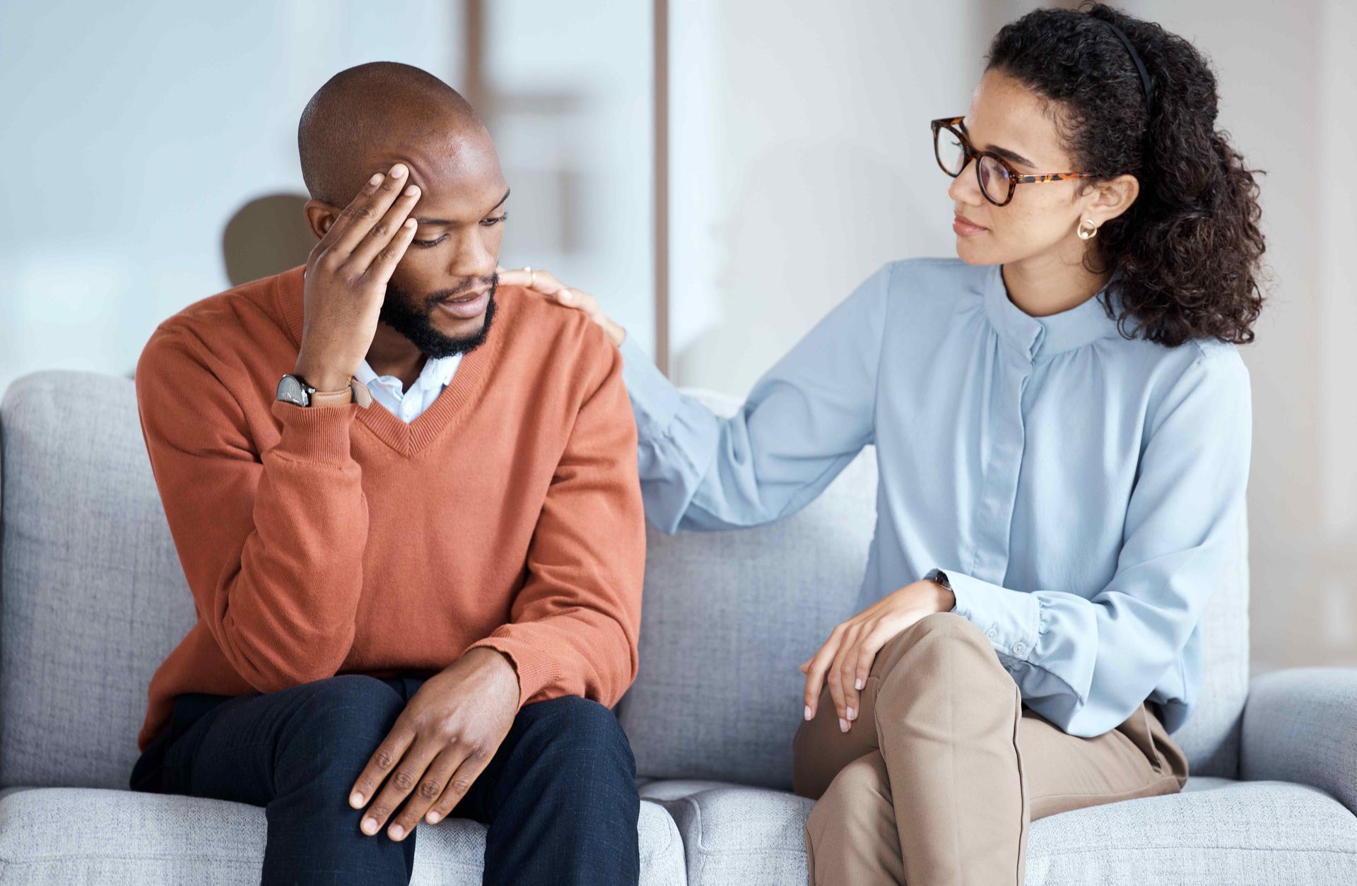 a woman is comforting a man who is sitting on a couch