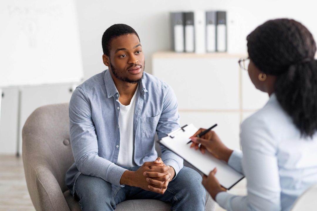 a man is sitting in a chair talking to a woman who is holding a clipboard