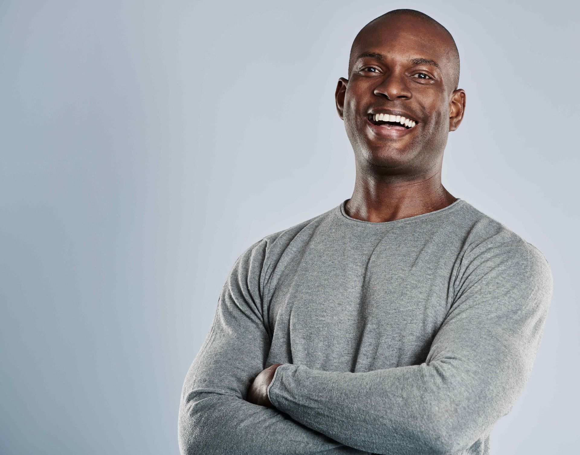 a man in a grey sweater is smiling with his arms crossed