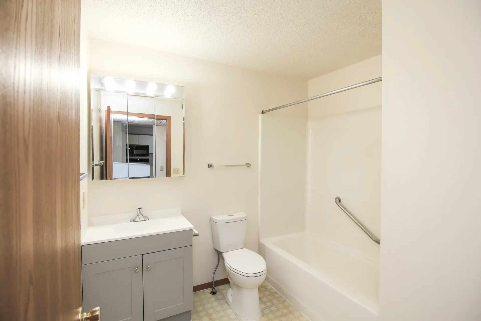 Small bathroom with a vanity, toilet, bathtub, mirror, and beige walls.