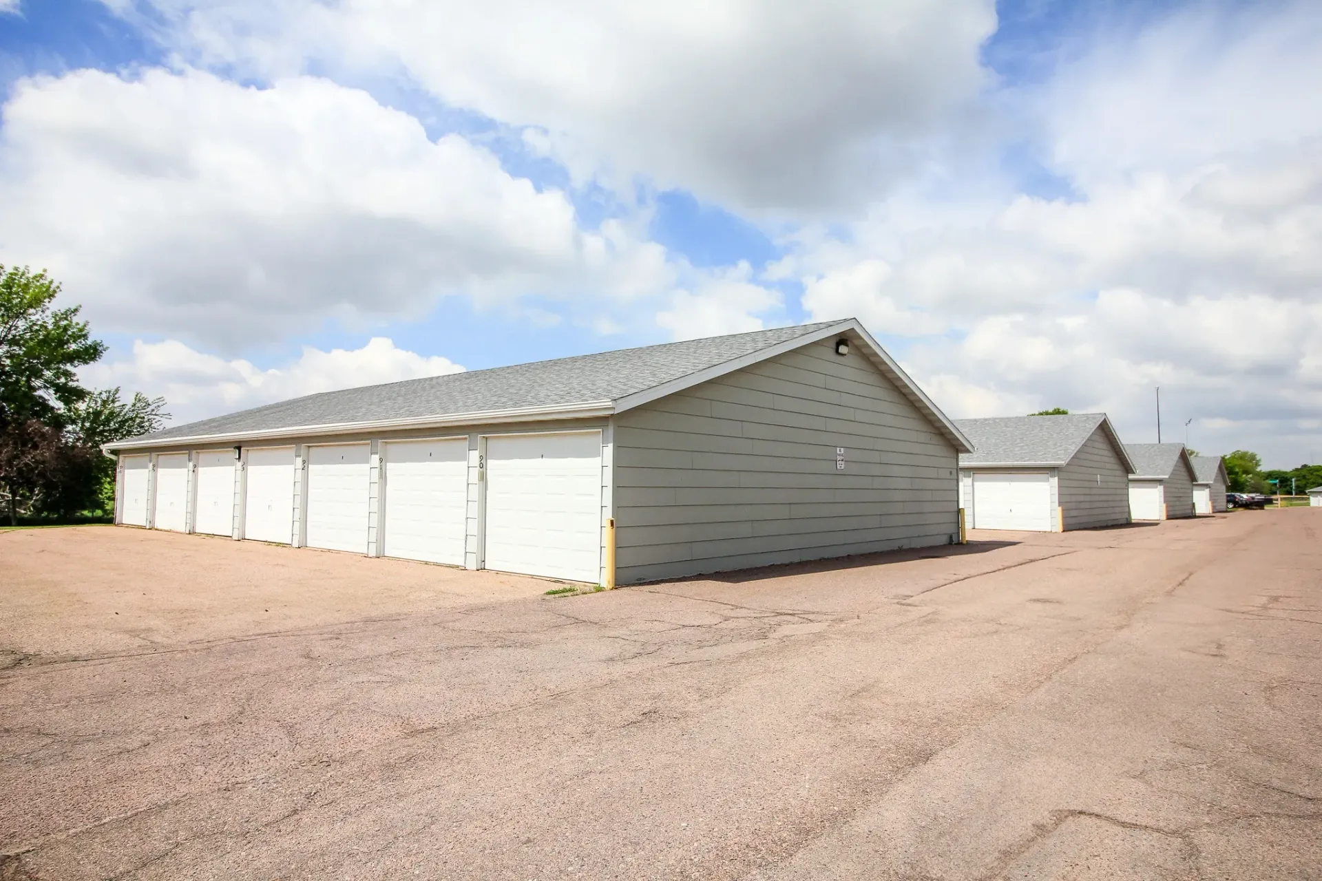 Row of white storage sheds on a gravel lot under a partly cloudy sky