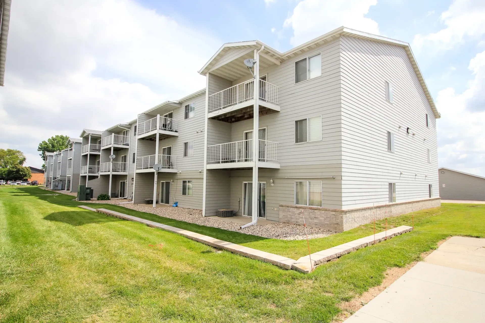 Gray apartment building with balconies beside a grassy lawn under a cloudy sky