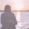 Person sitting by the water at sunset, with the sun reflecting on a calm shoreline.