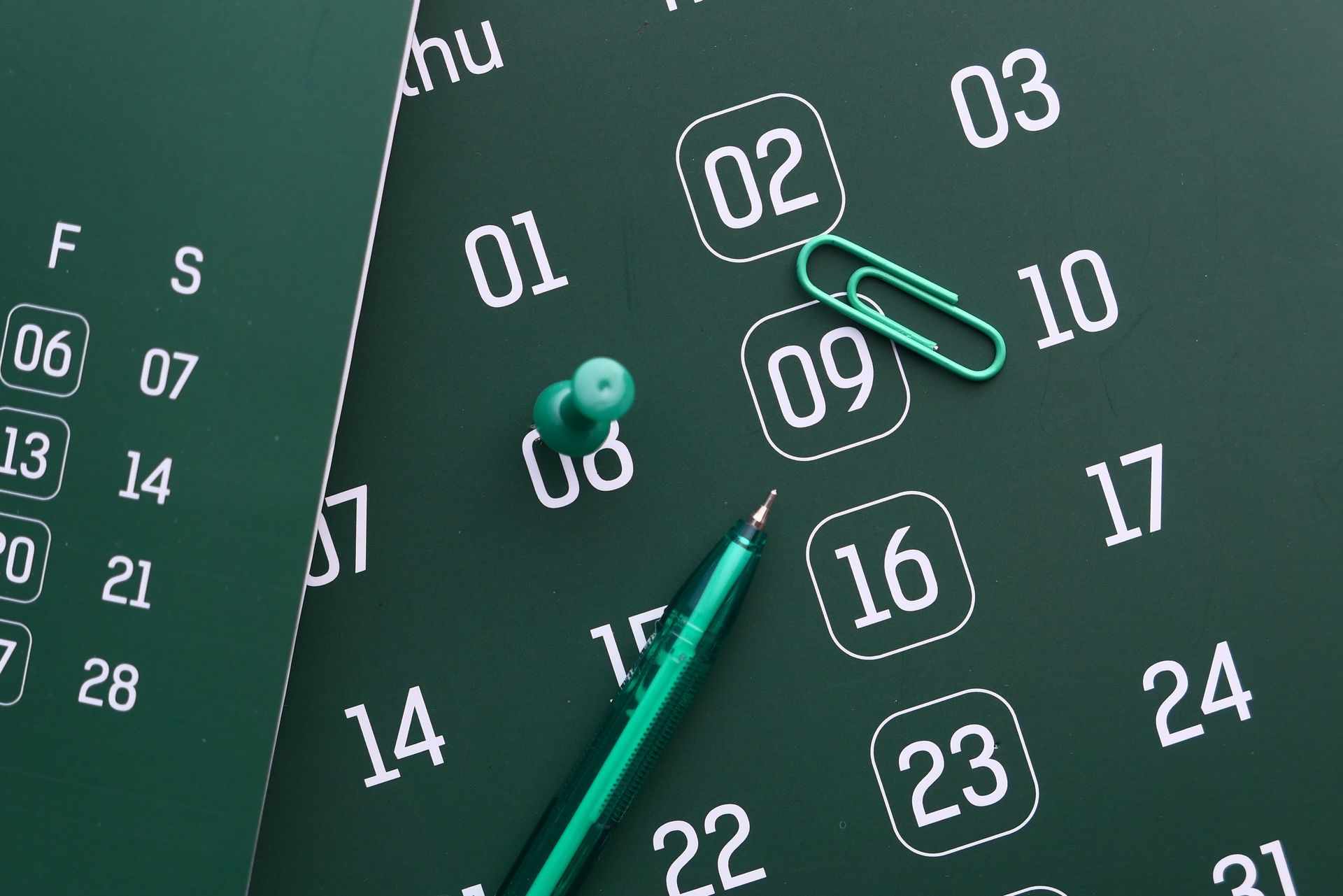Green calendar planner with pinned notes, circled dates, and a pen marking a date
