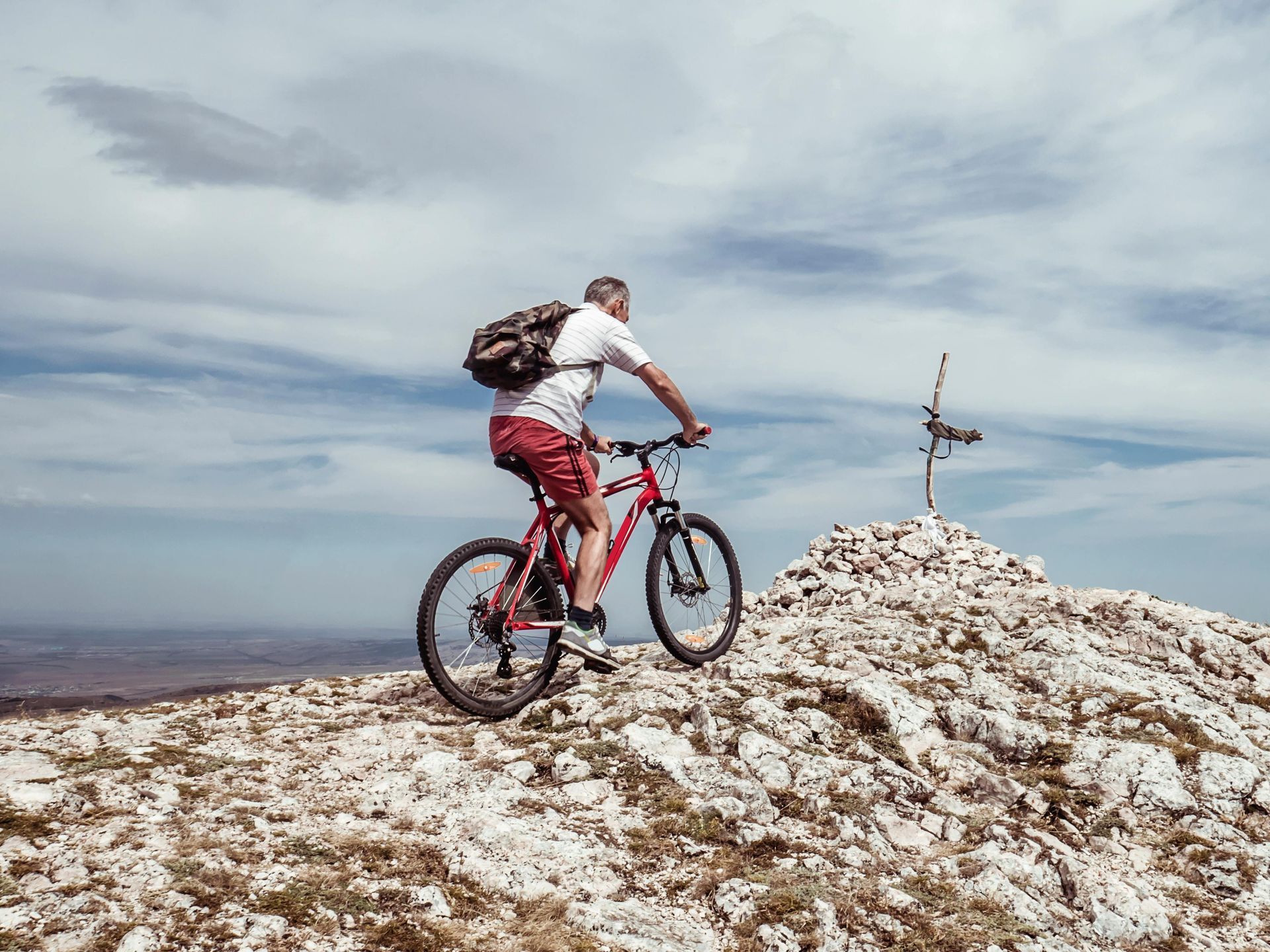 Cyclist rides a red mountain bike up a rocky hill under a cloudy sky.