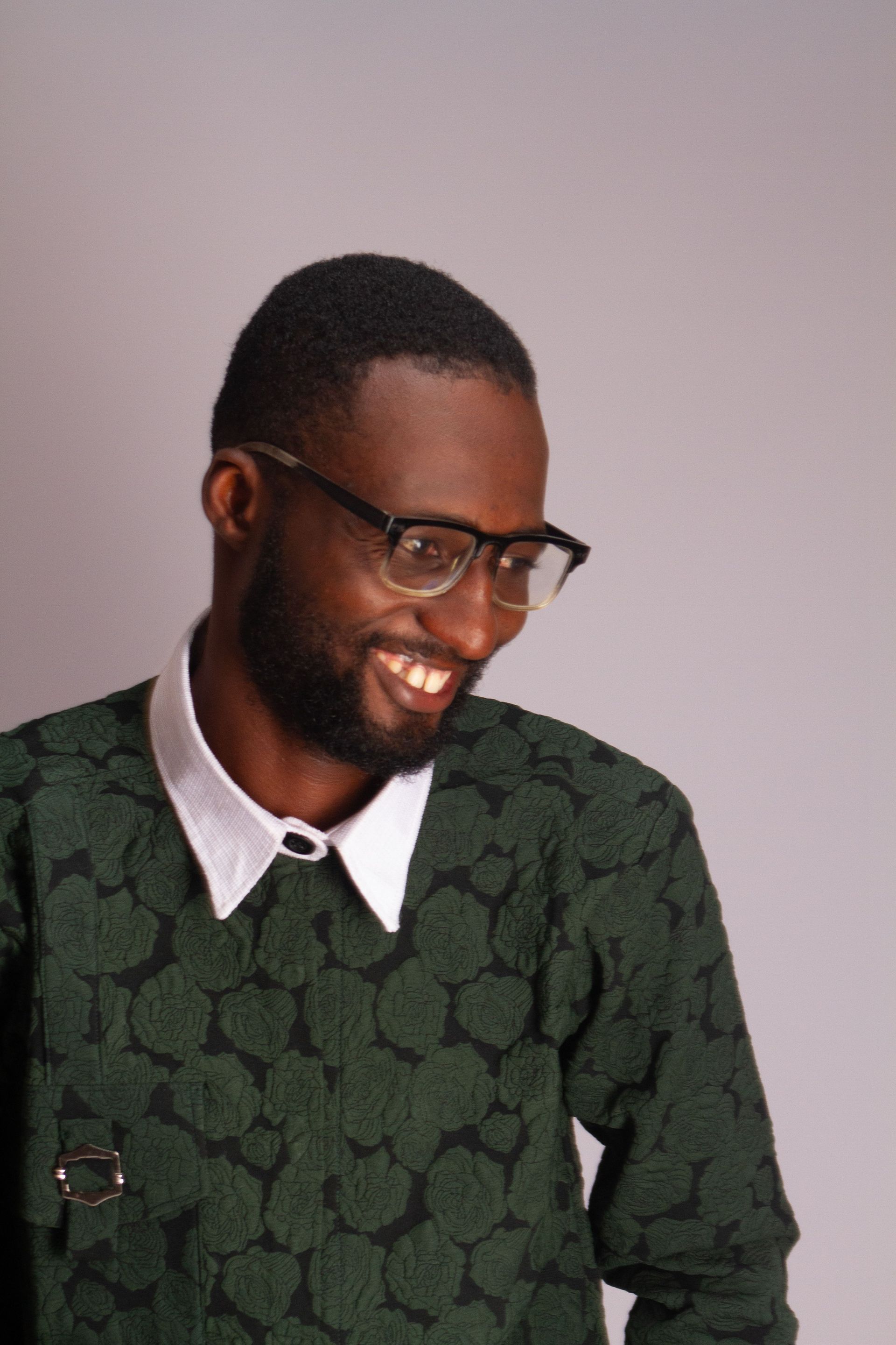 Smiling man in glasses and green patterned sweater against a plain gray background