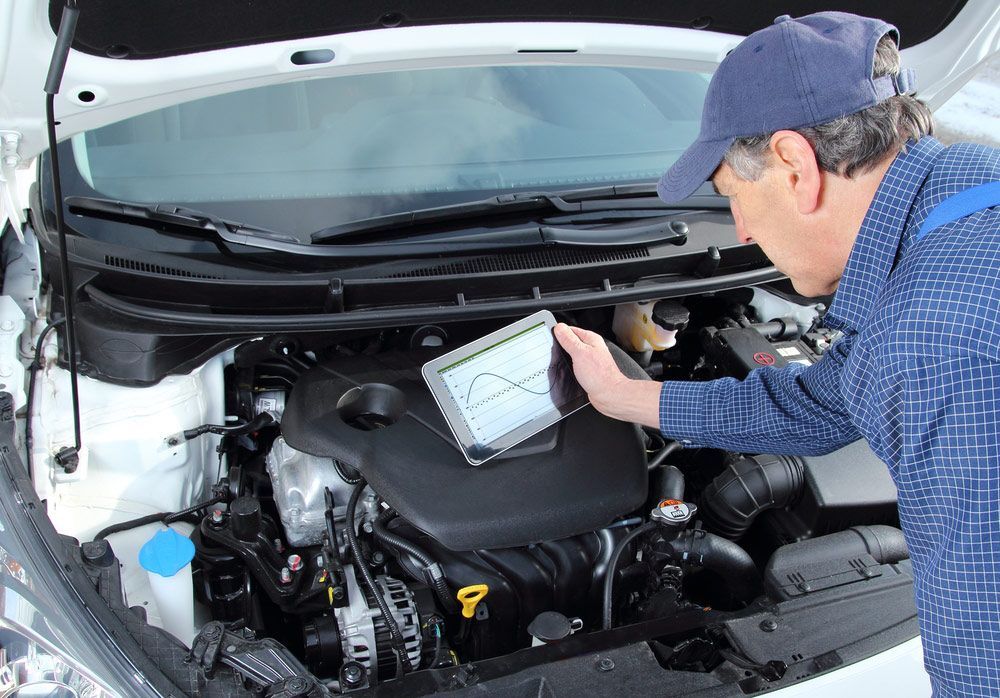 A Man Is Working on The Engine of A Car with A Tablet — A & K Auto Electrical & Air Conditioning in Tamworth, NSW