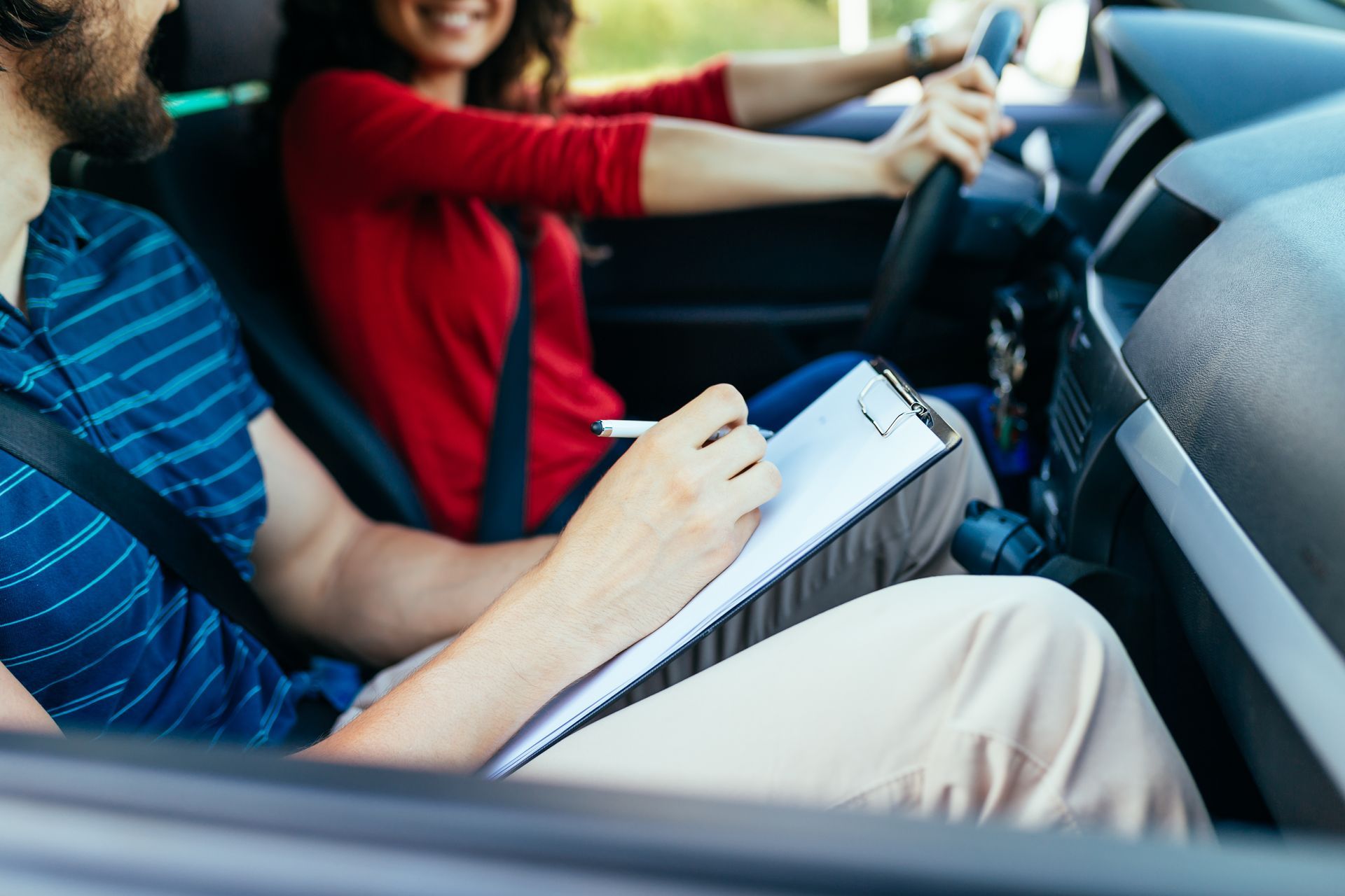 Person driving car while another takes notes on clipboard. Person driving car while another takes notes on clipboard.