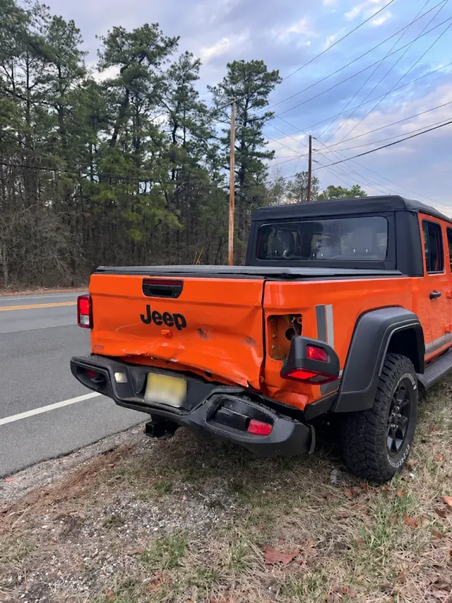 Orange Jeep Gladiator with damaged tailgate and rear bumper before repair at Auto Craftman and Collision