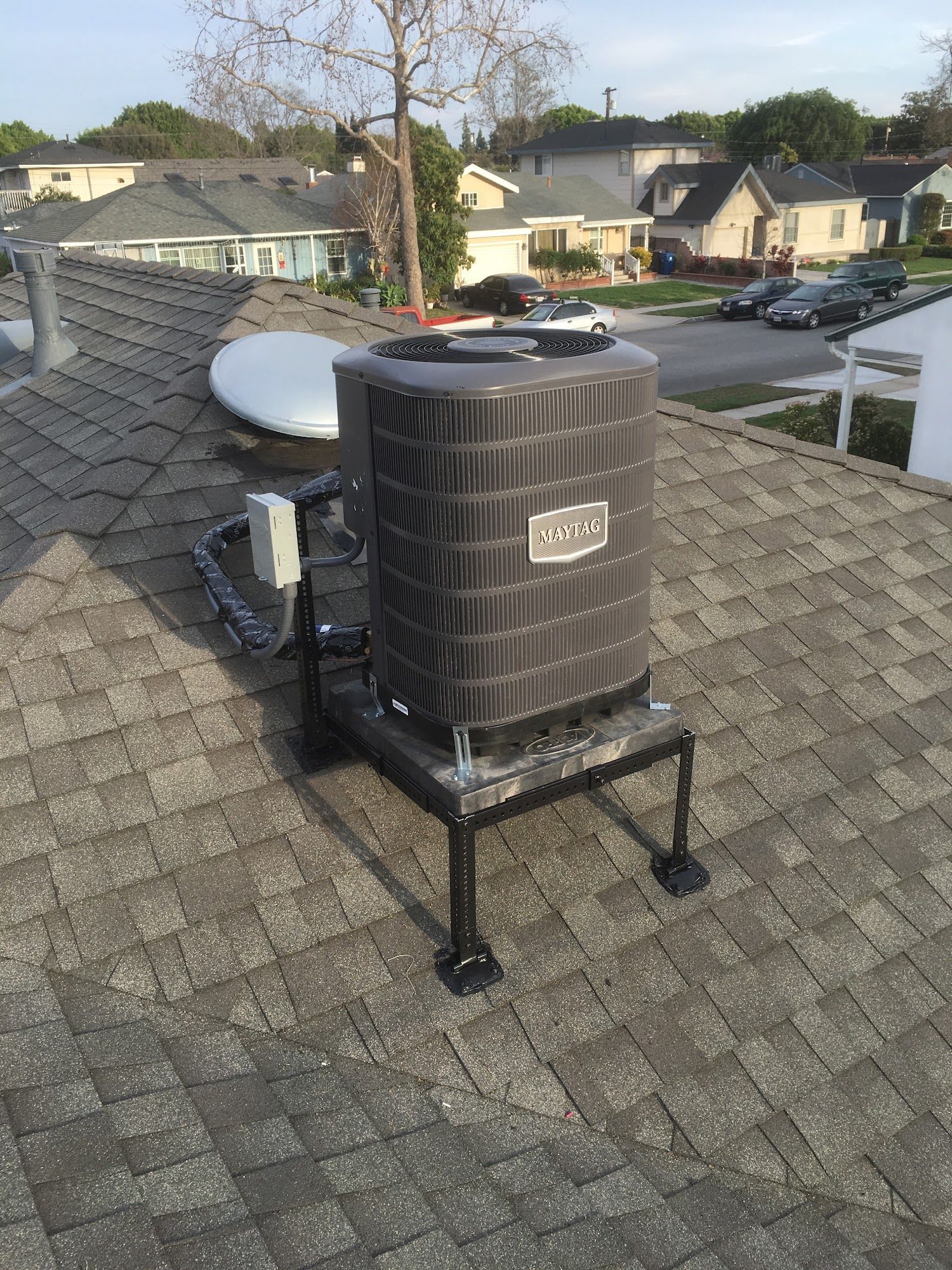 Air conditioning unit on a rooftop, black and gray, with surrounding neighborhood houses.