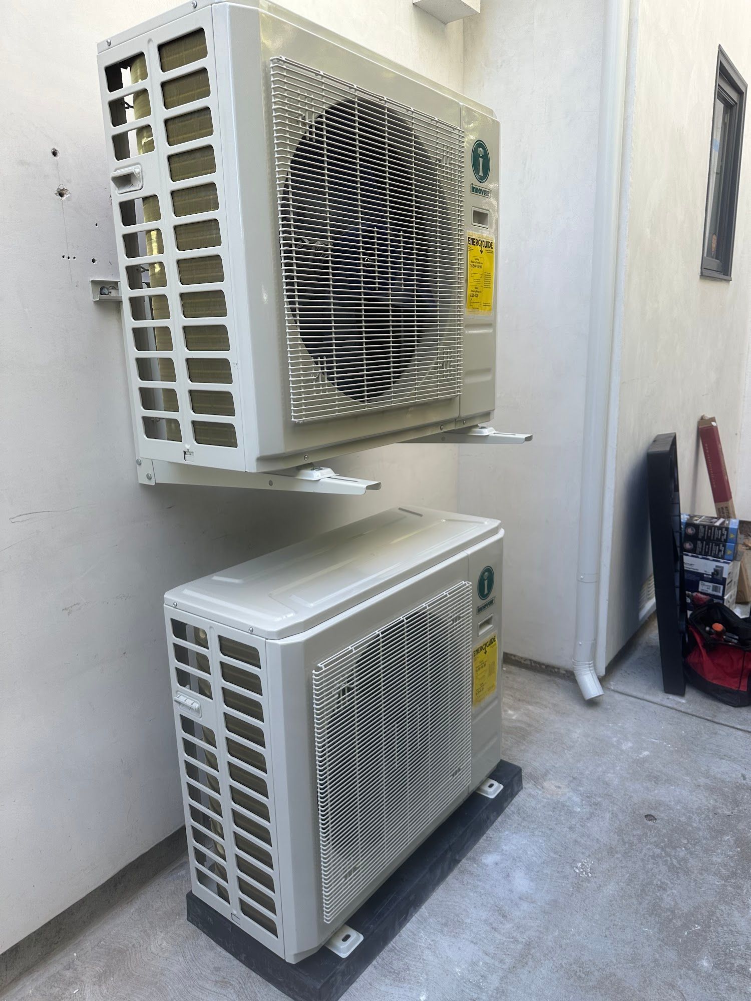 Two white air conditioning units mounted on an exterior wall, one above the other.