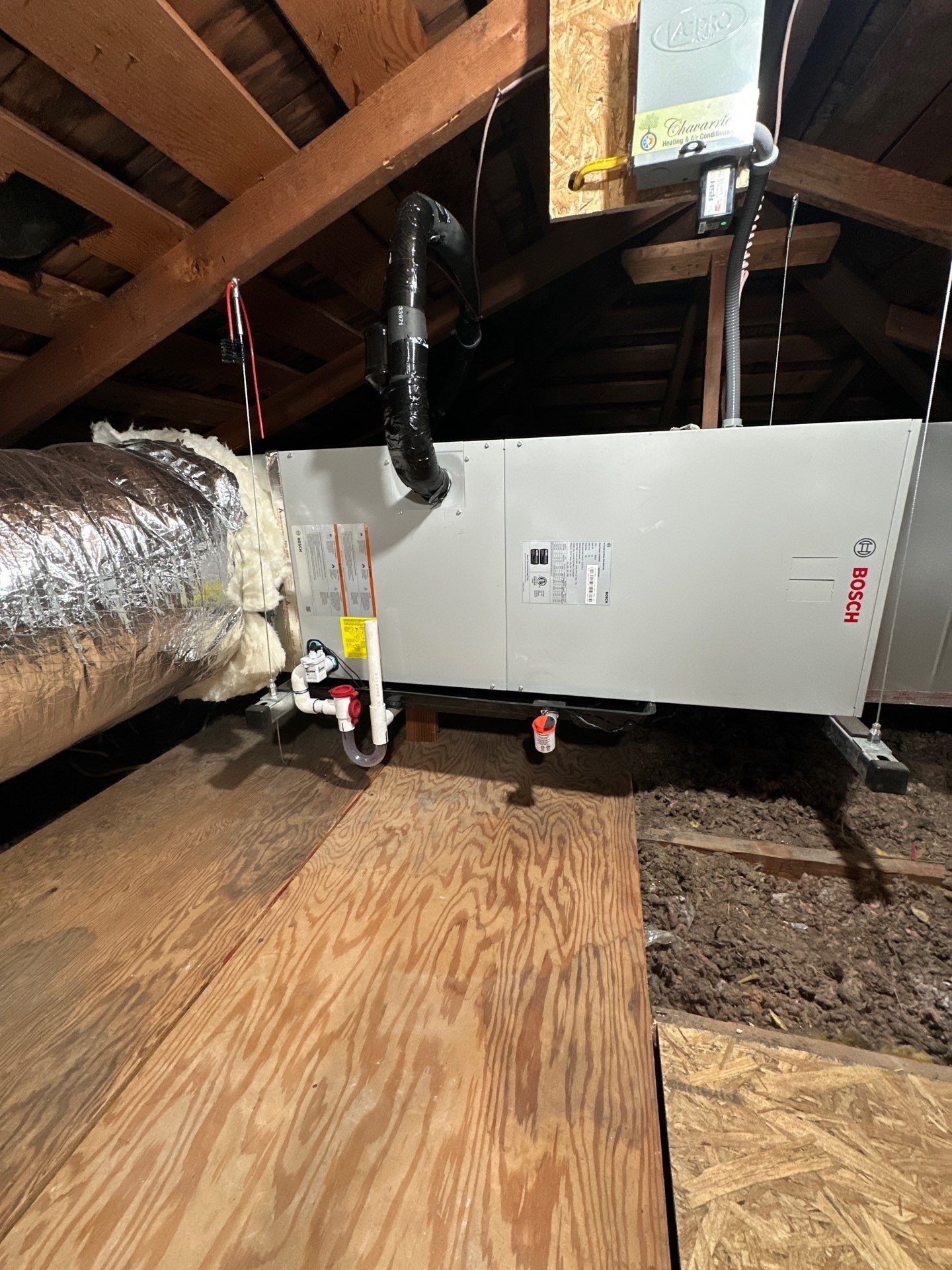 HVAC unit in an attic with ductwork, insulation, and wooden structure.