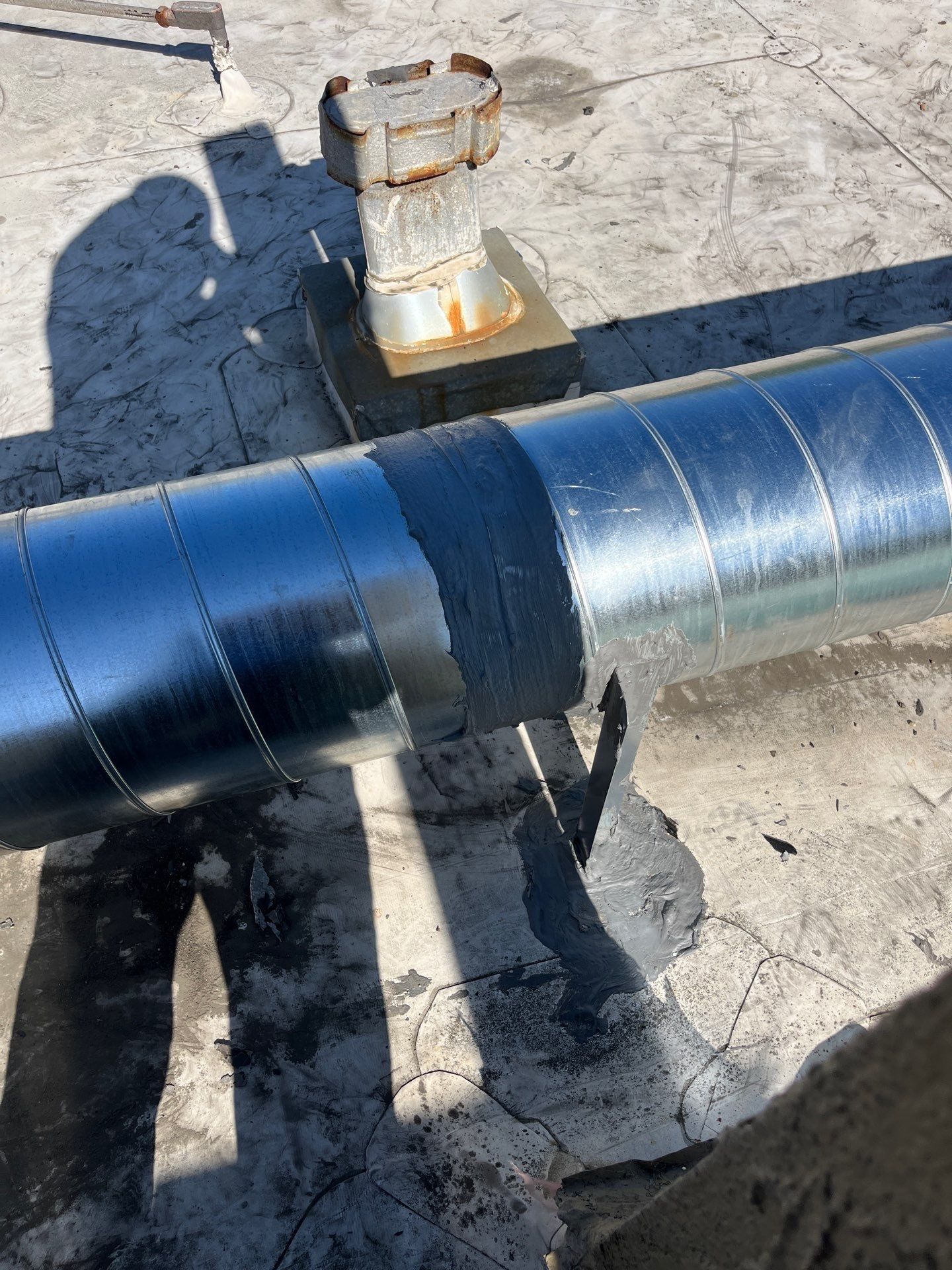 Metal ductwork on a rooftop, with a rusty vent and dark sealant.