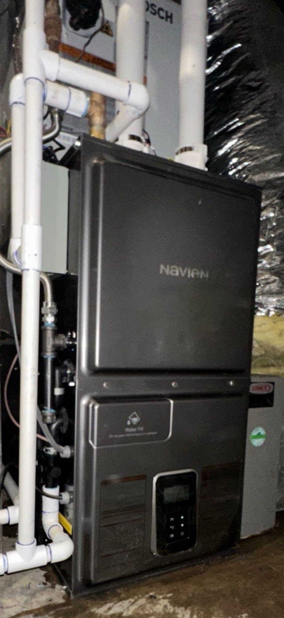A Navien tankless water heater with white pipes, sitting in a basement setting.