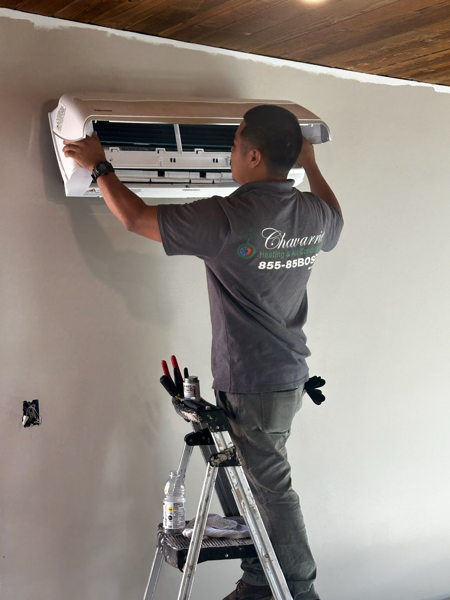 Person installing an air conditioning unit on a wall, standing on a ladder.
