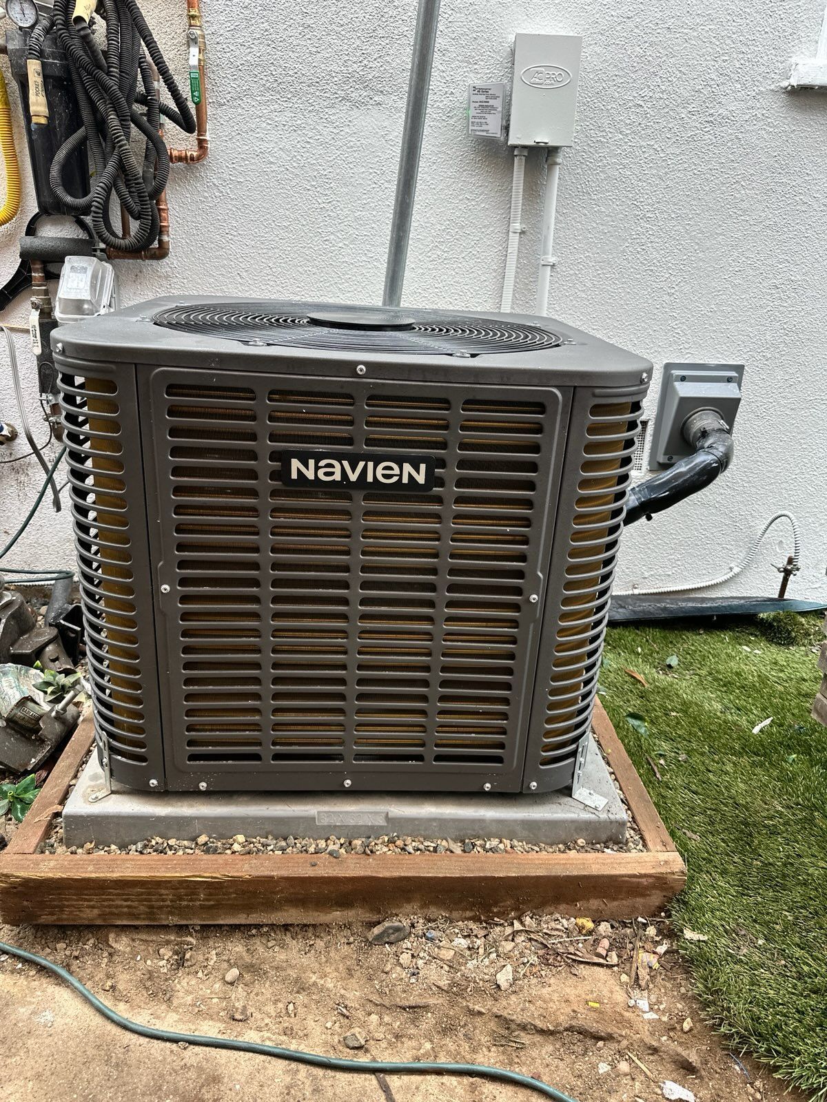 Navien air conditioning unit on a concrete base, mounted outdoors next to a wall.