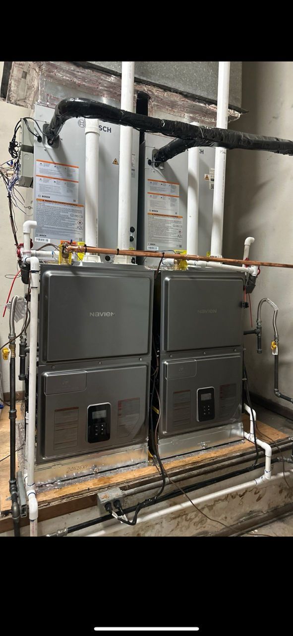 Two stacked HVAC units with white piping in a utility room.