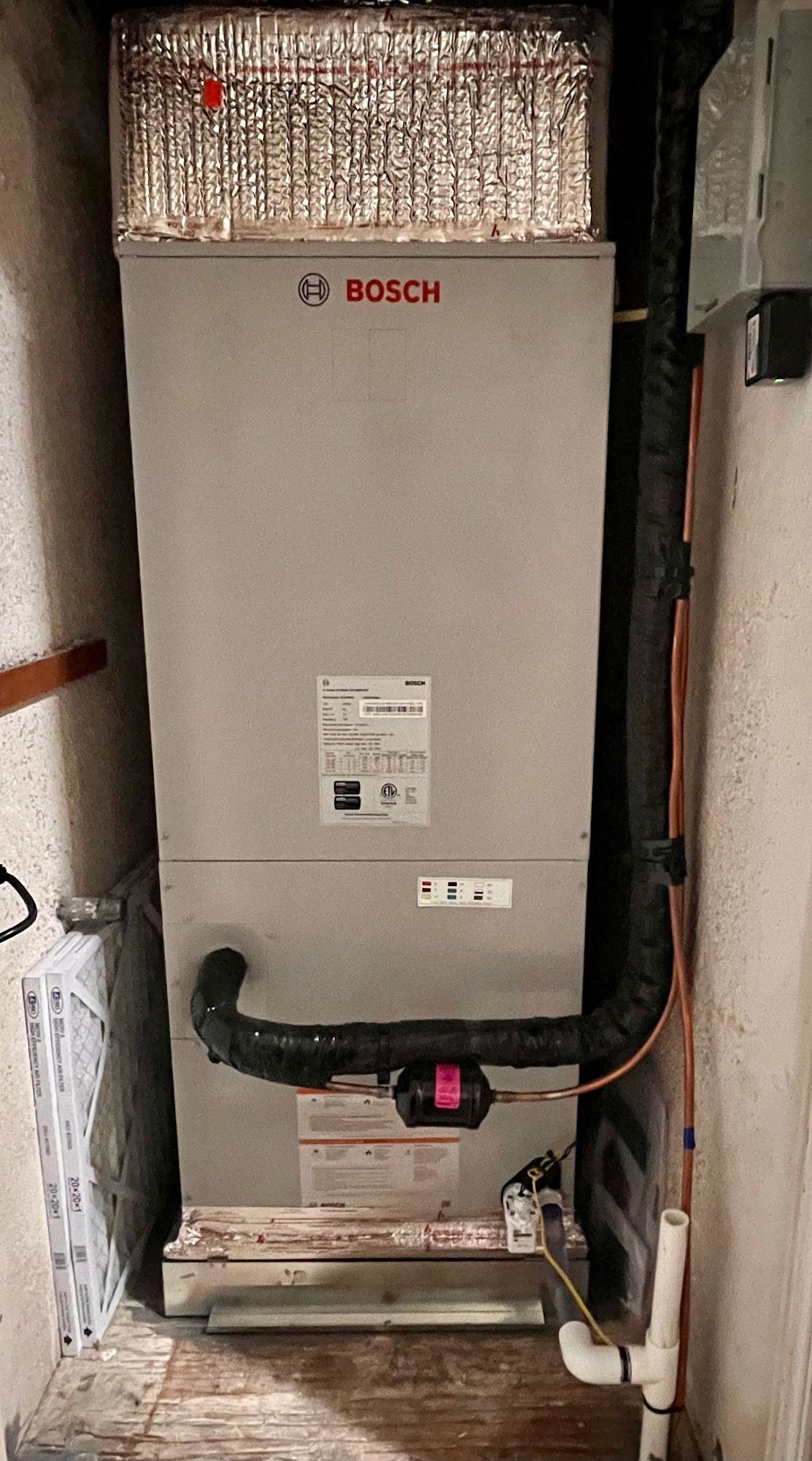 Bosch furnace in a utility room. Gray metal unit with black exhaust pipe and white gas line.