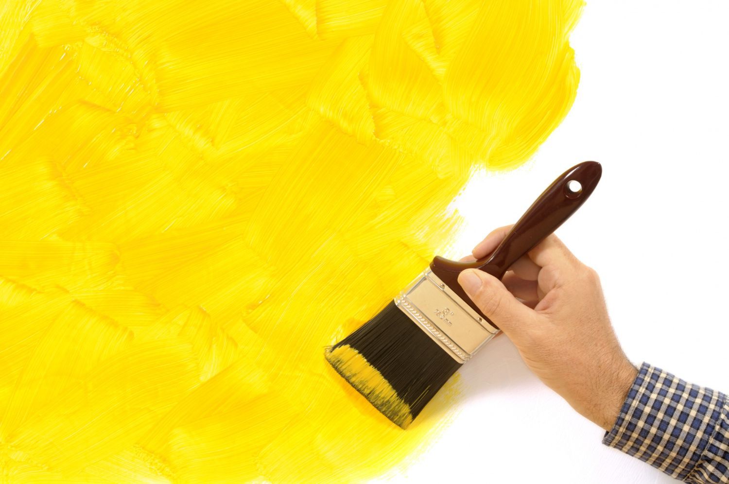 Hand using a paintbrush to apply bright yellow paint on a white surface