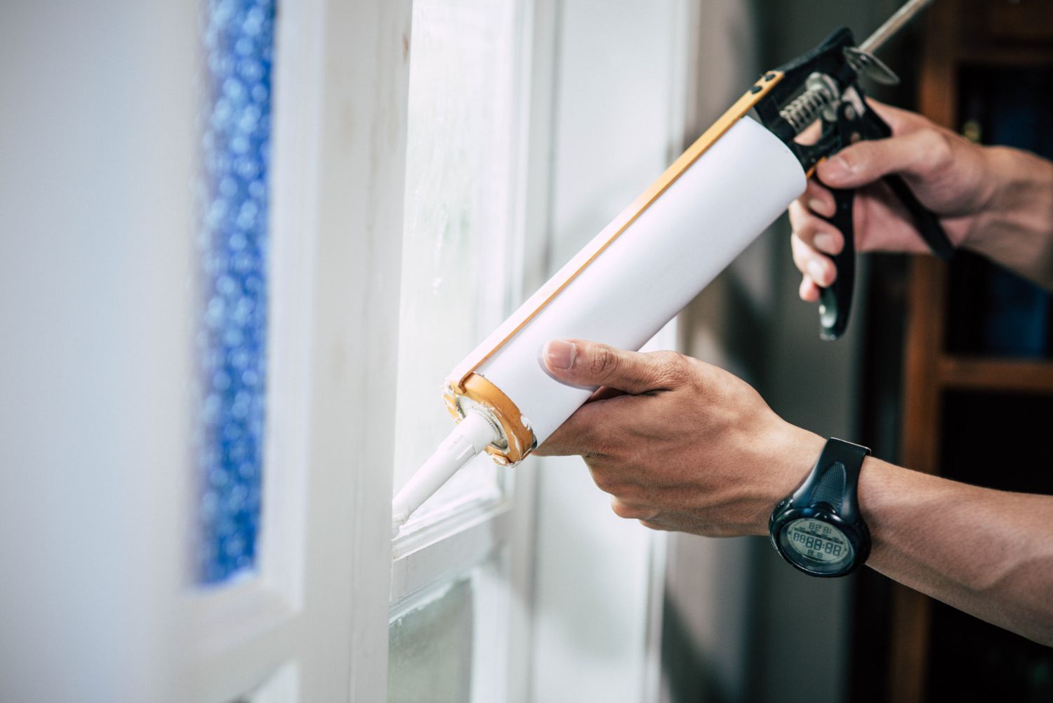 Hand applying white caulk with a caulking gun along a window frame