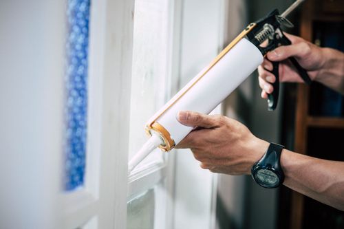 Hand applying white caulk with a caulking gun along a window frame