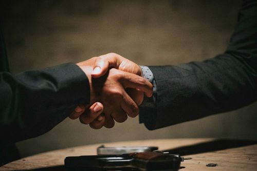 Two people in dark suits shaking hands over a conference table