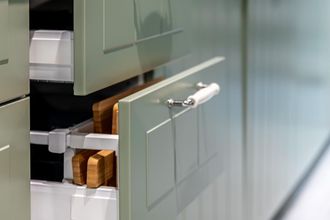 Open cabinet drawer with white handles and wooden contents in a kitchen-like setting