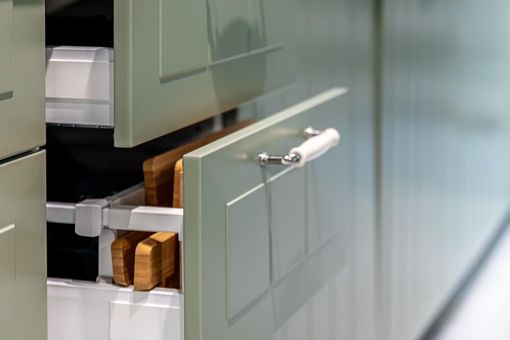 Open cabinet drawer with white handles and wooden contents in a kitchen-like setting