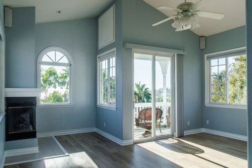 Bright empty living room with blue walls, fireplace, arched window, and sliding glass doors to a patio