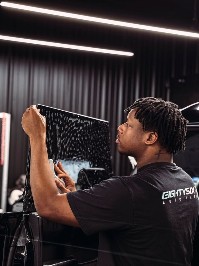 A person is applying tinted window film to a car window.