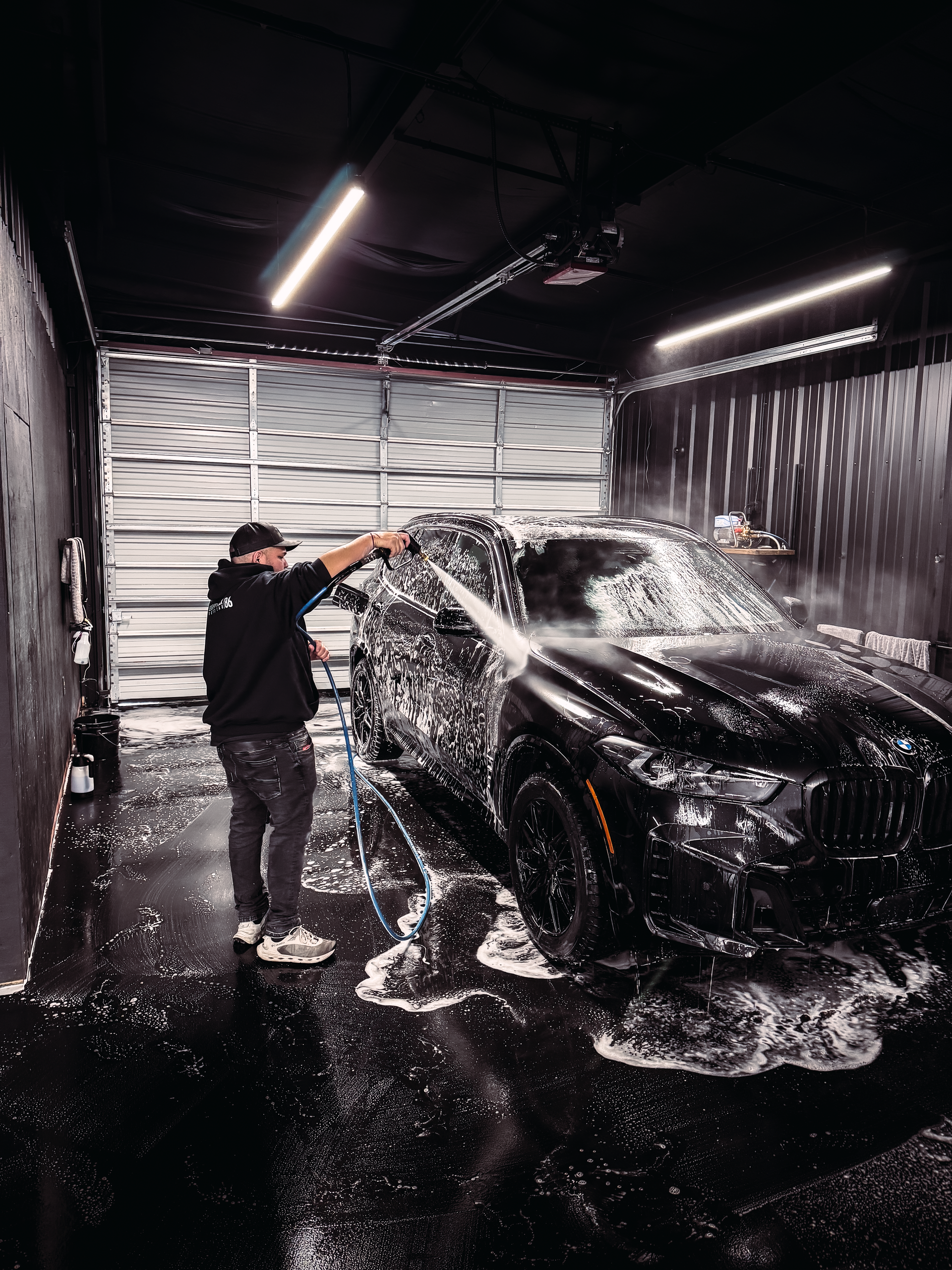 A man is washing a red tesla model 3 in a garage.