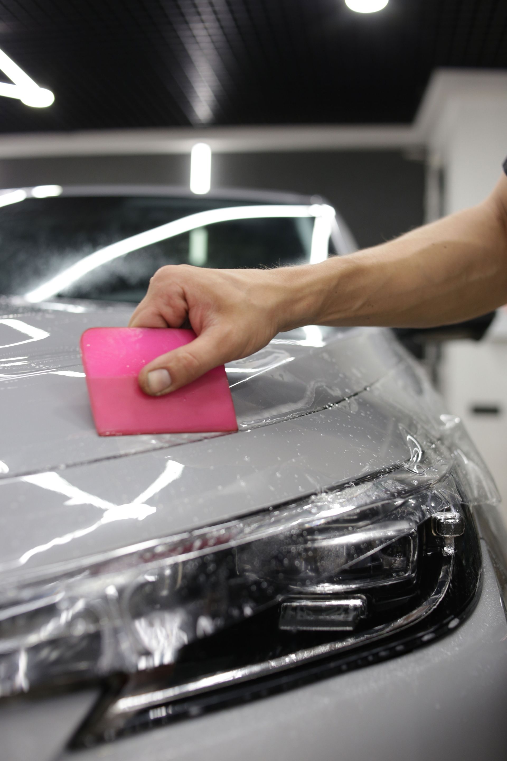 A person is applying a protective film to the hood of a car.