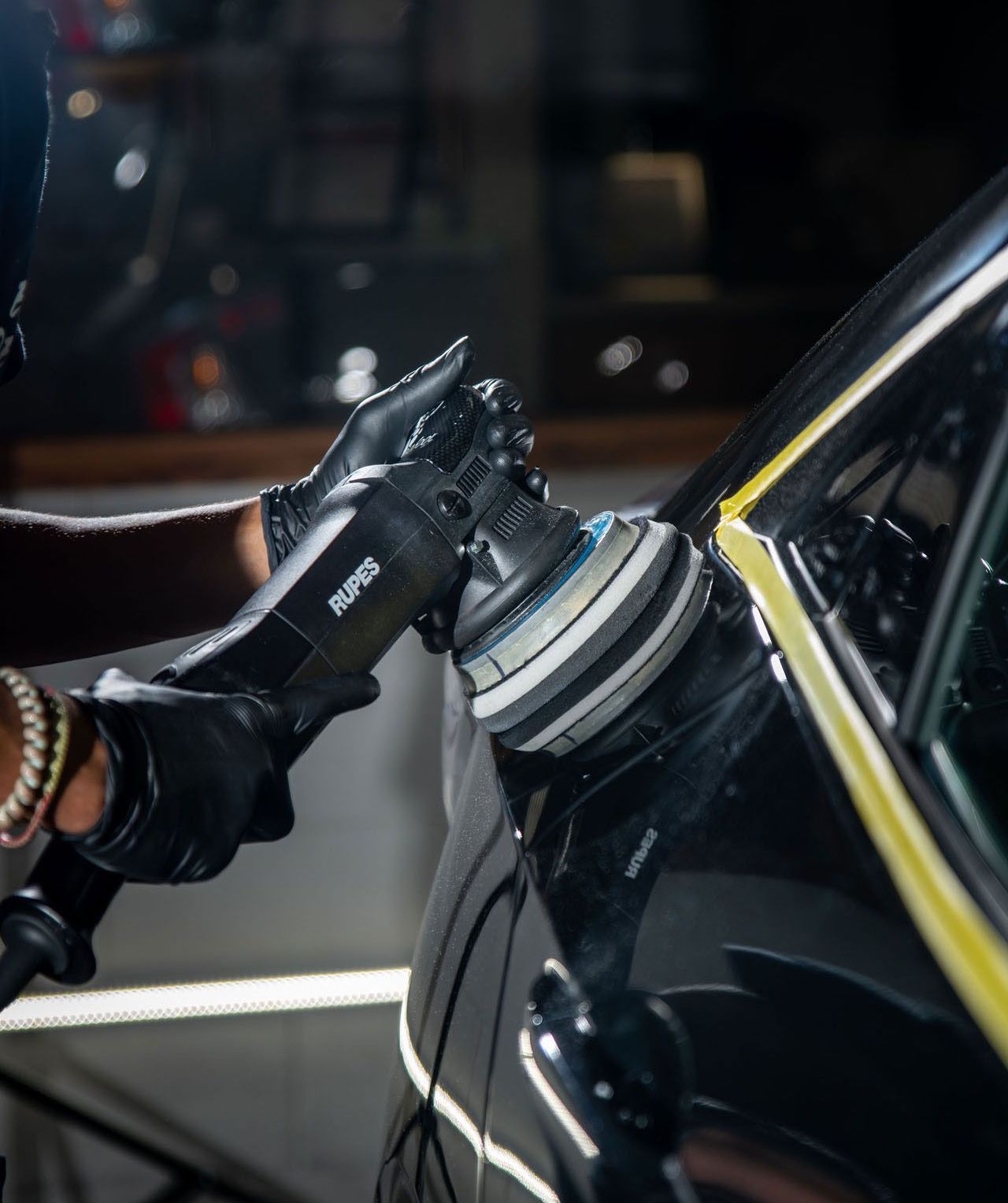 A person is polishing a black car with a machine that says rupes on it