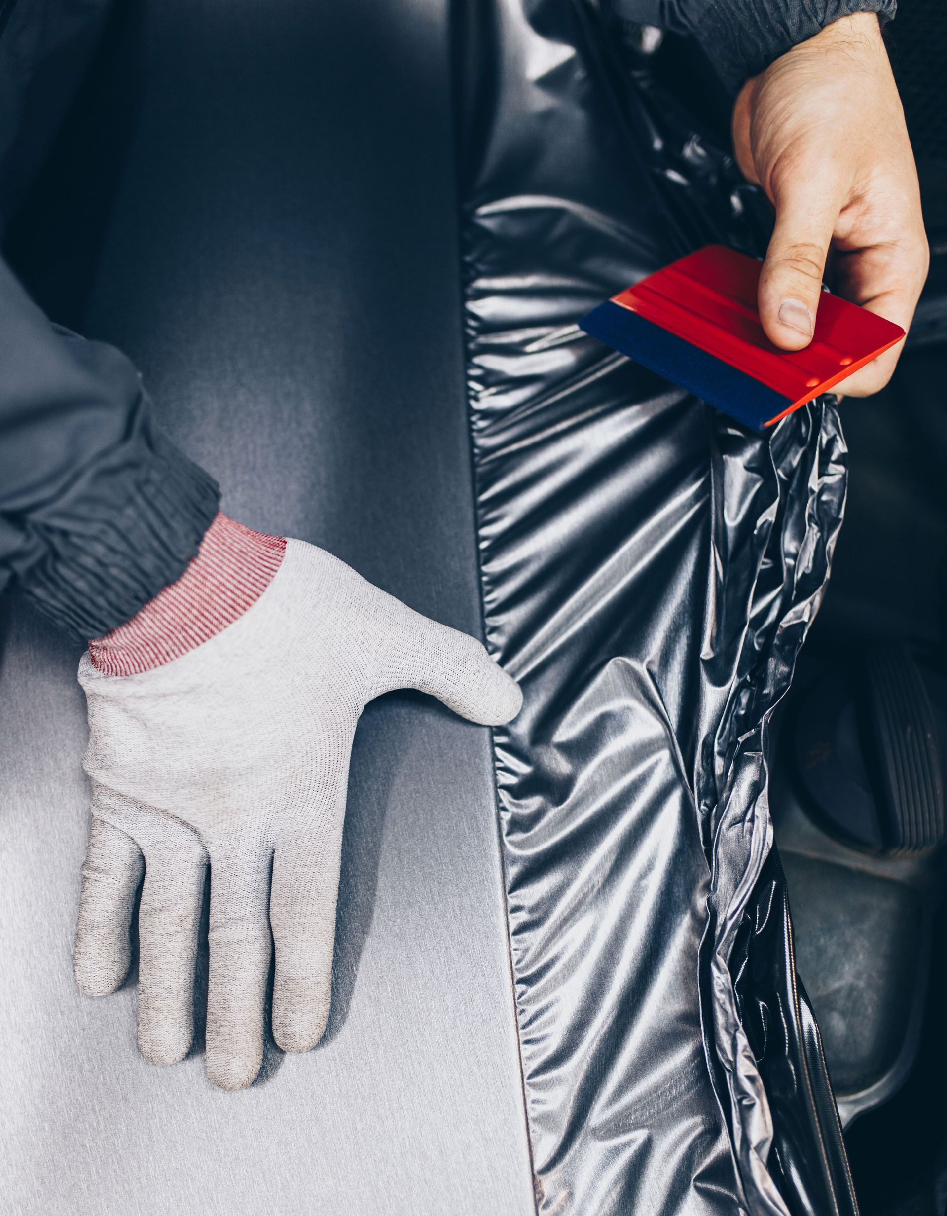 A person is wrapping a car with a glove and a spatula.