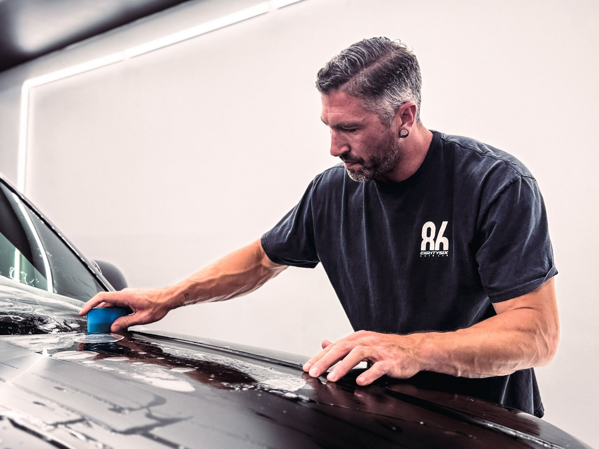 Man polishing a black car hood with a blue buffer in a garage