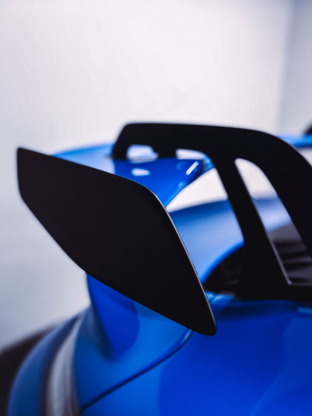 Blue sports car rear with black spoiler.