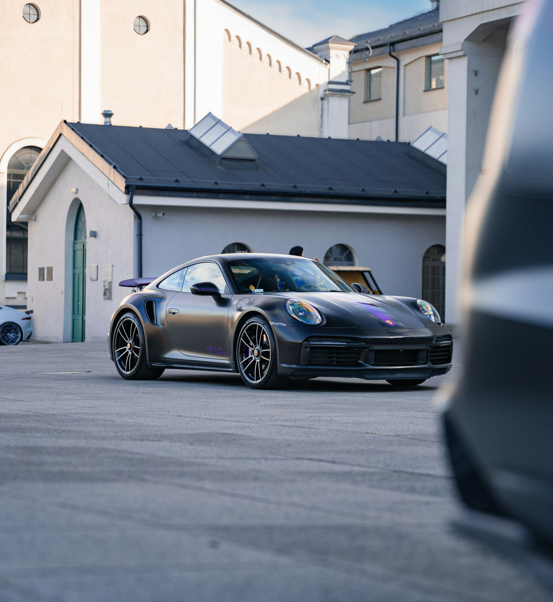 Dark gray Porsche 911 parked in a courtyard with buildings in the background.
