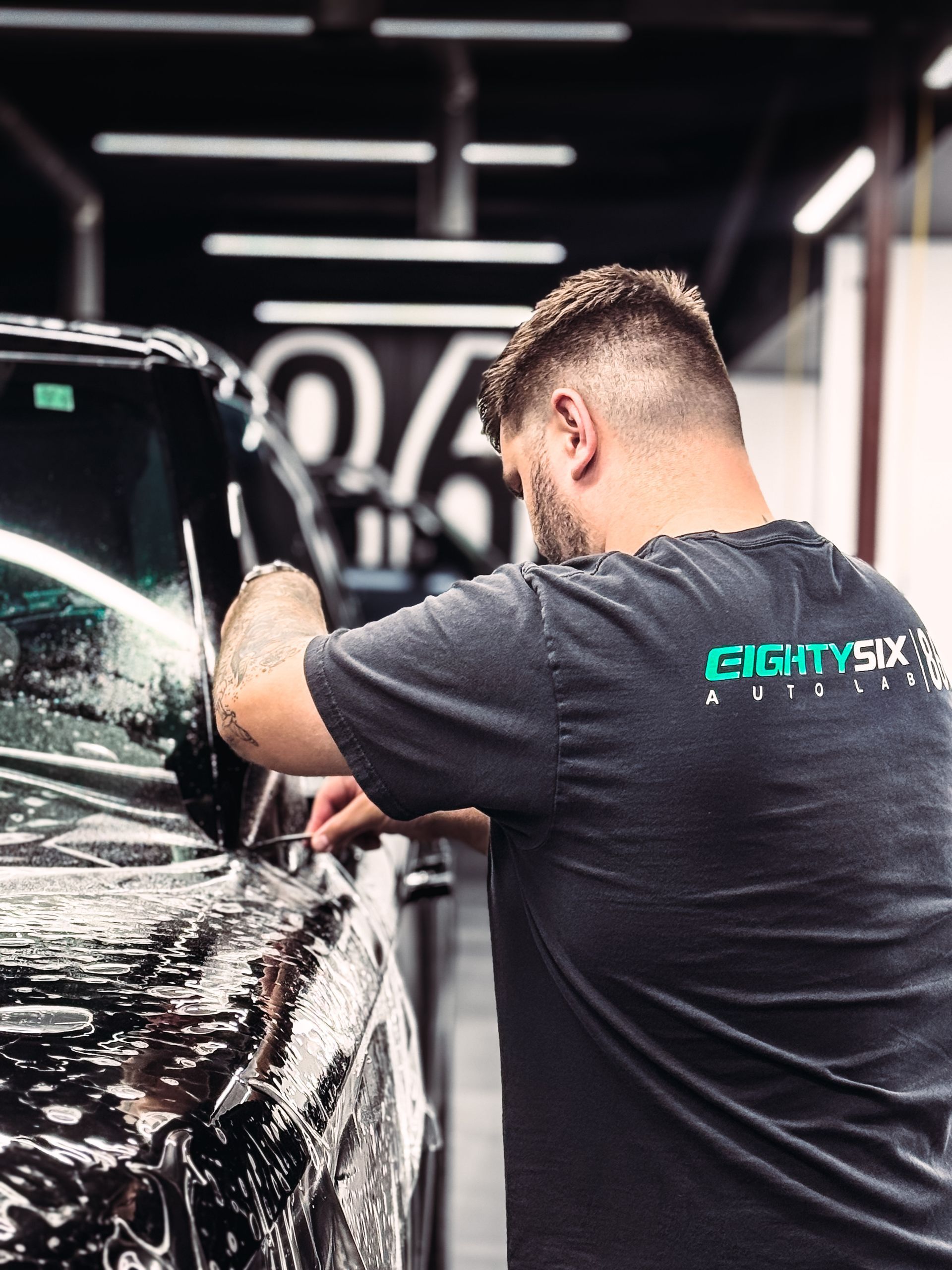Detailing technician polishing a black car inside a bright auto shop