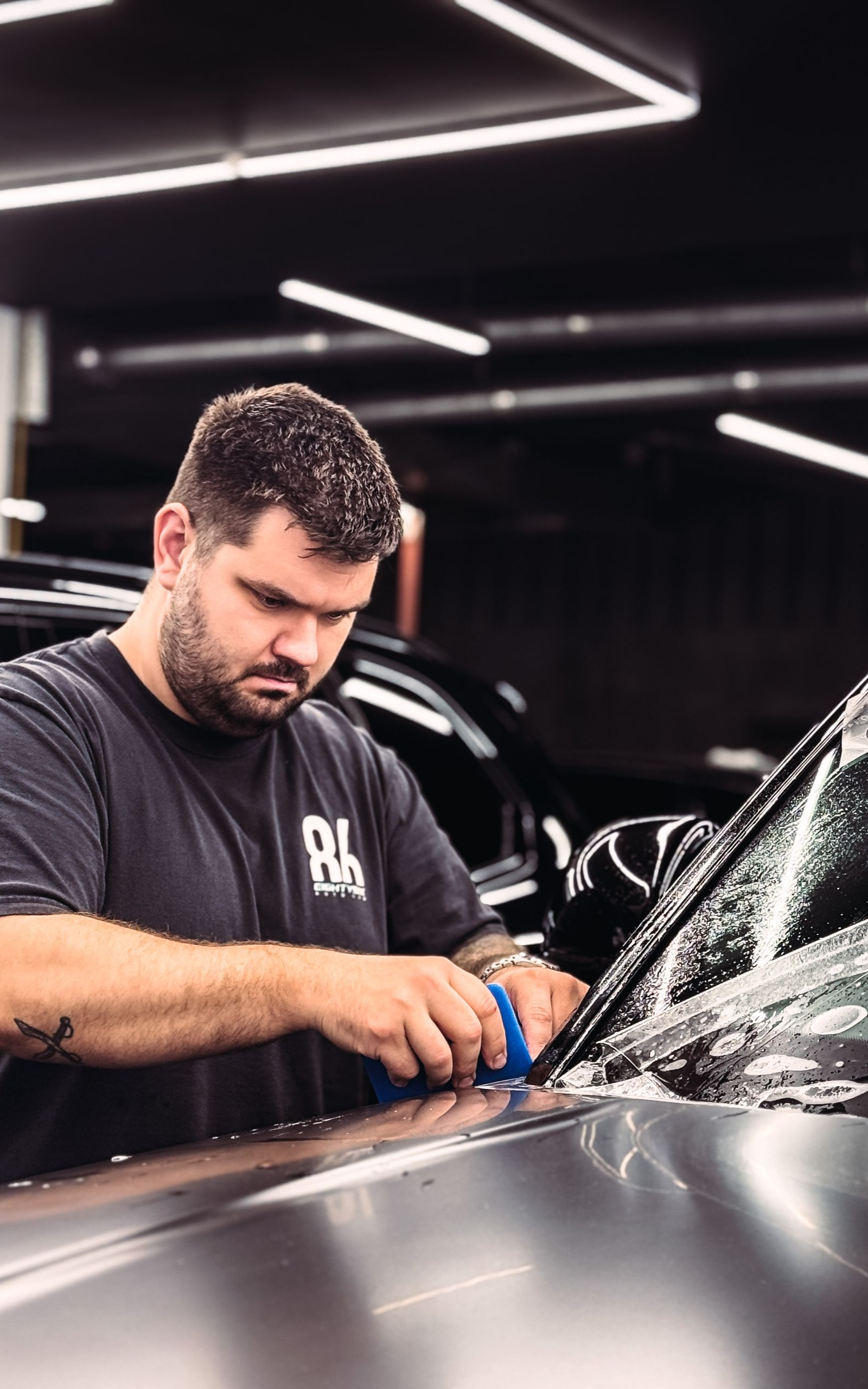 Detailer polishing a dark car in a modern workshop