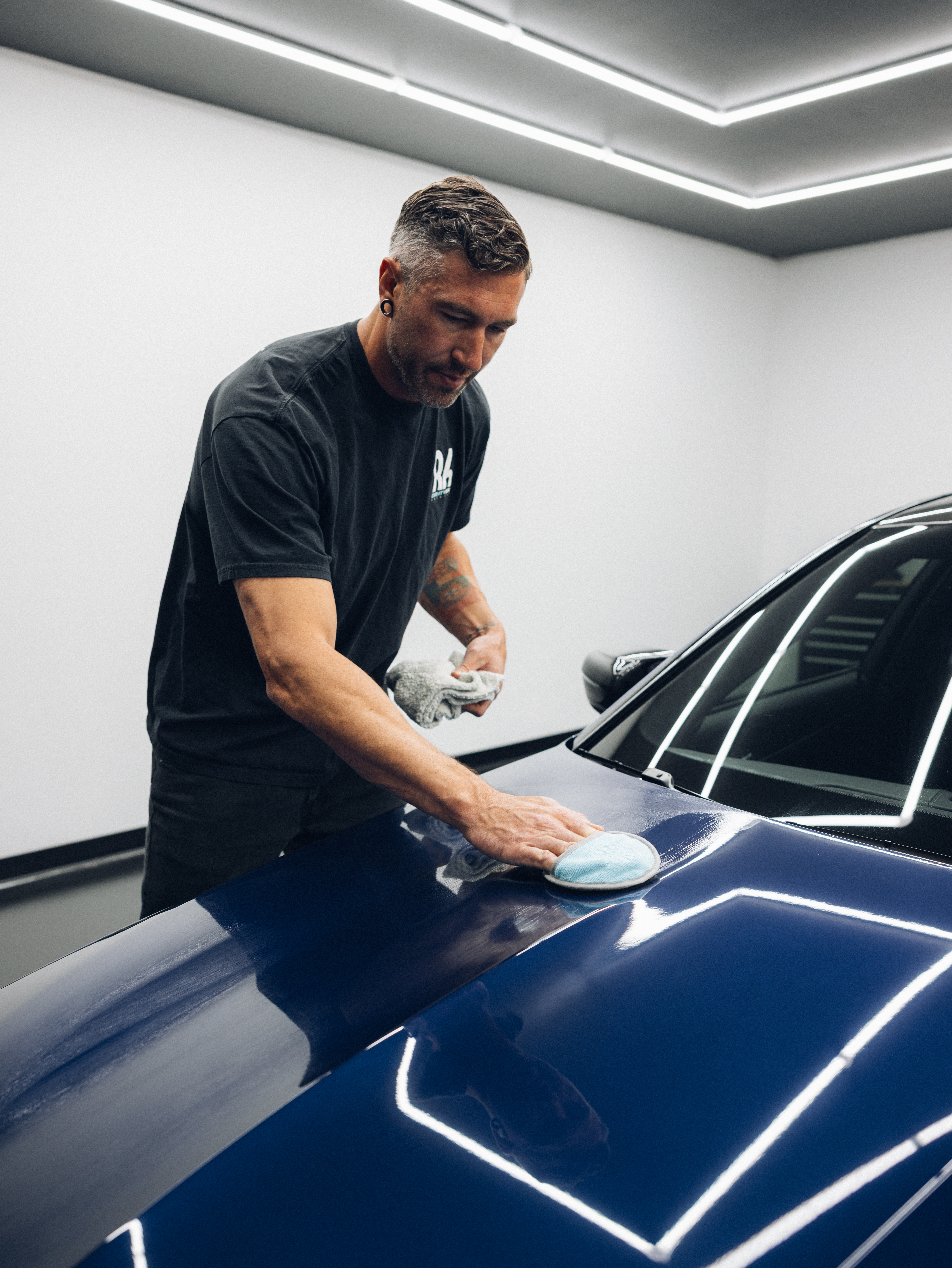 Man polishing a blue car in a bright garage.