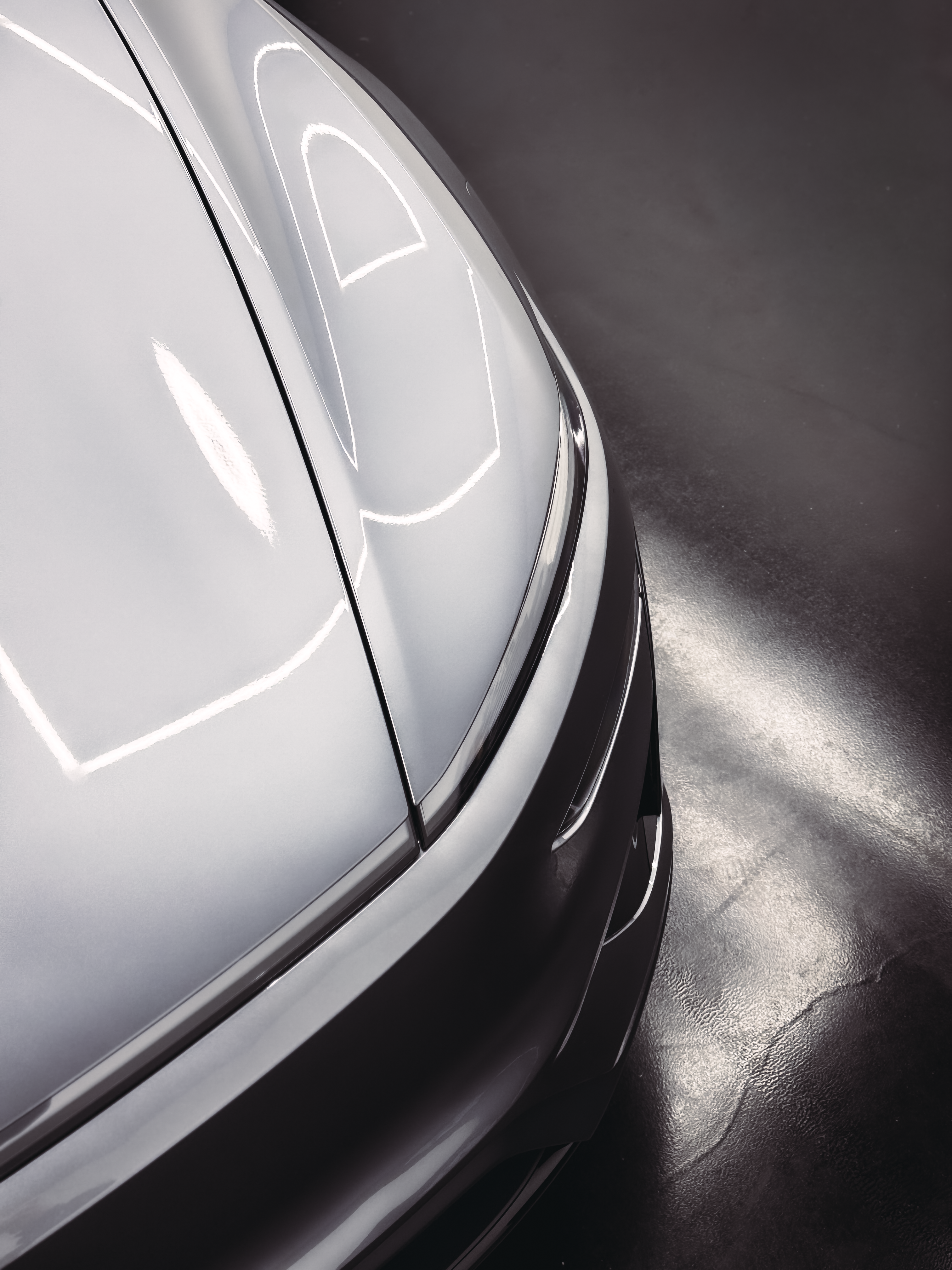 Shiny silver car hood reflecting overhead lights, against a dark background.