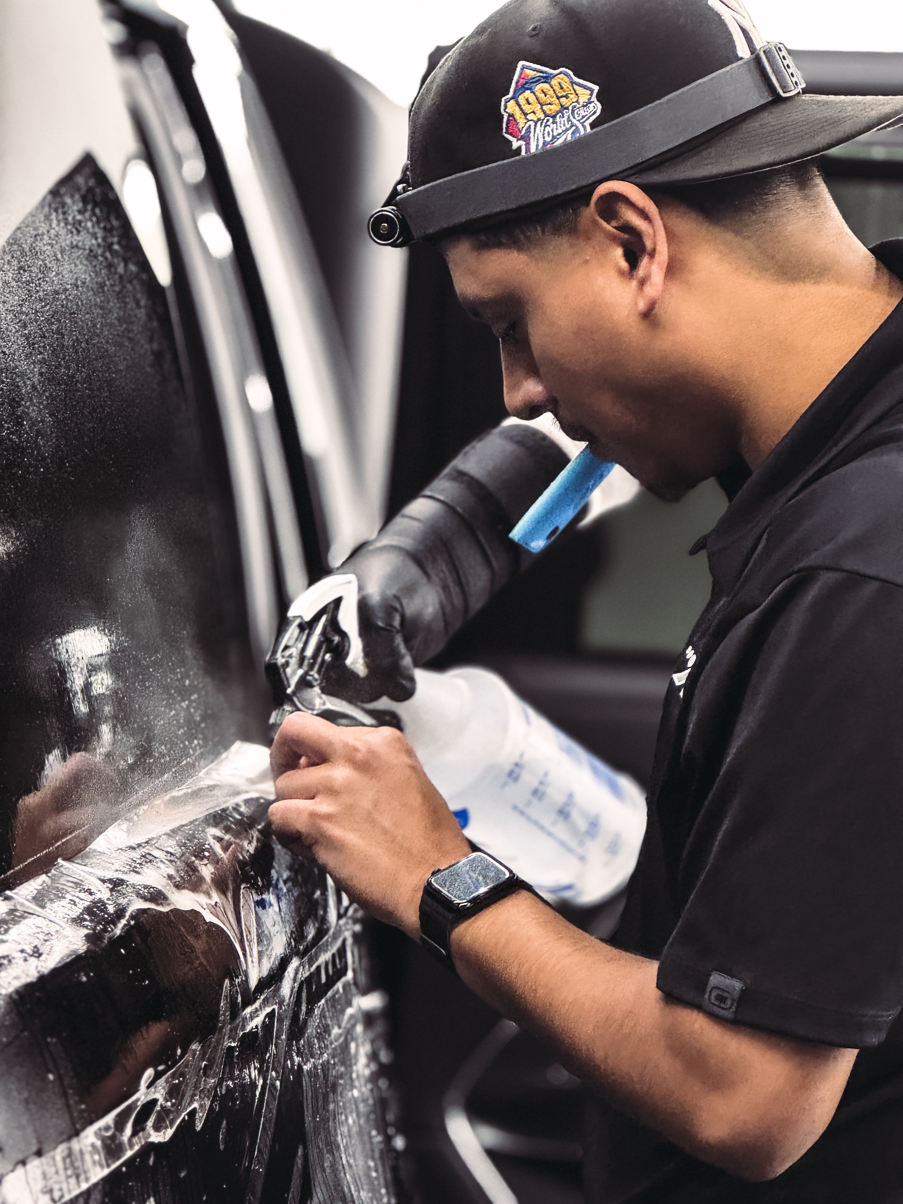 Person applies window tinting to a car door, wearing gloves and a headlamp.