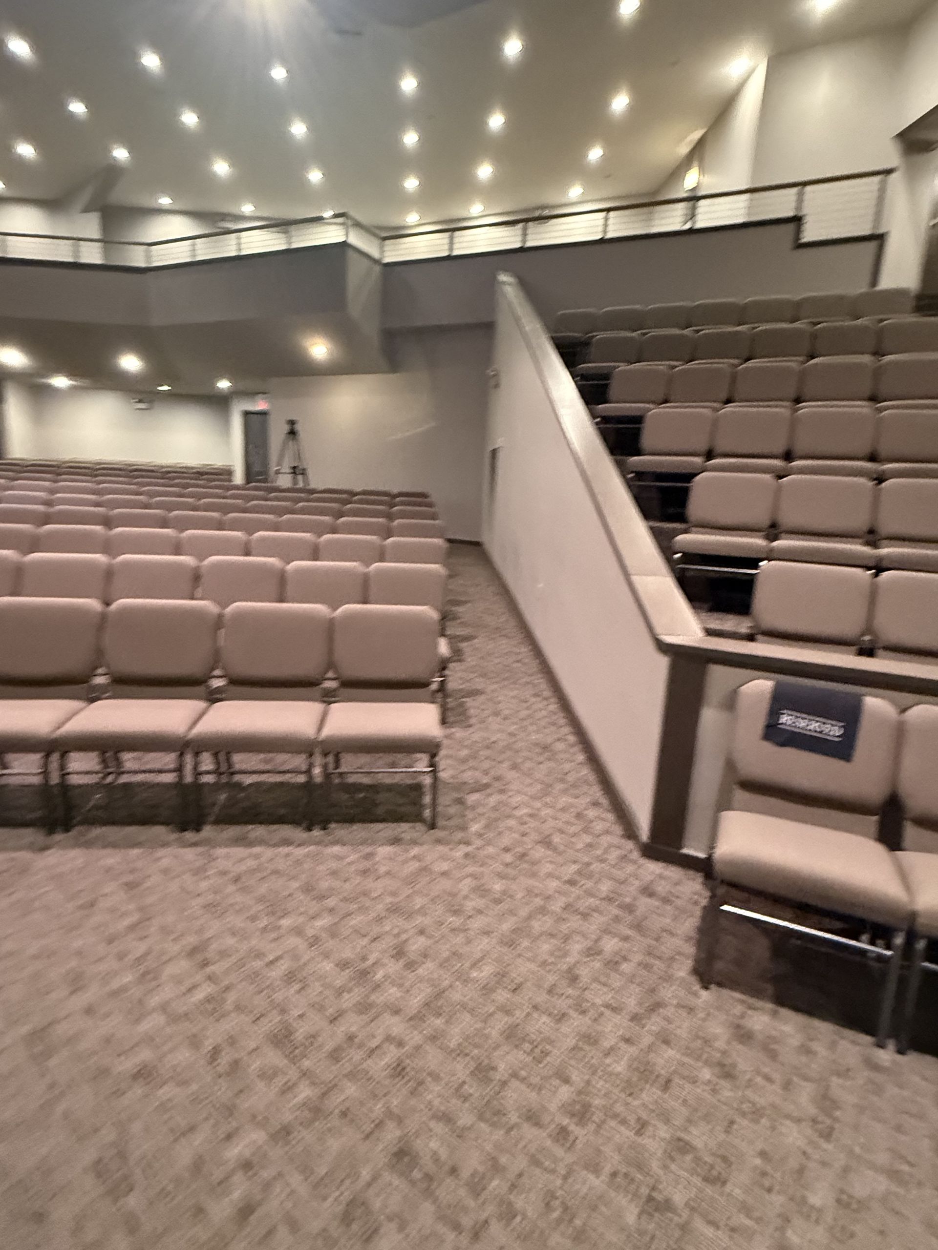 Empty auditorium seating with tan chairs and carpeted aisles under recessed lights