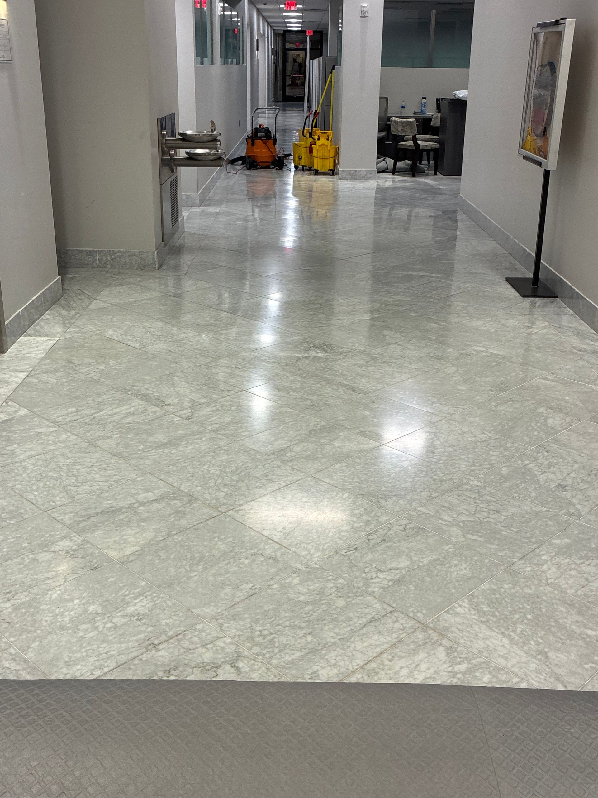 Empty indoor hallway with polished marble floor, columns, and a few cleaning carts in the distance