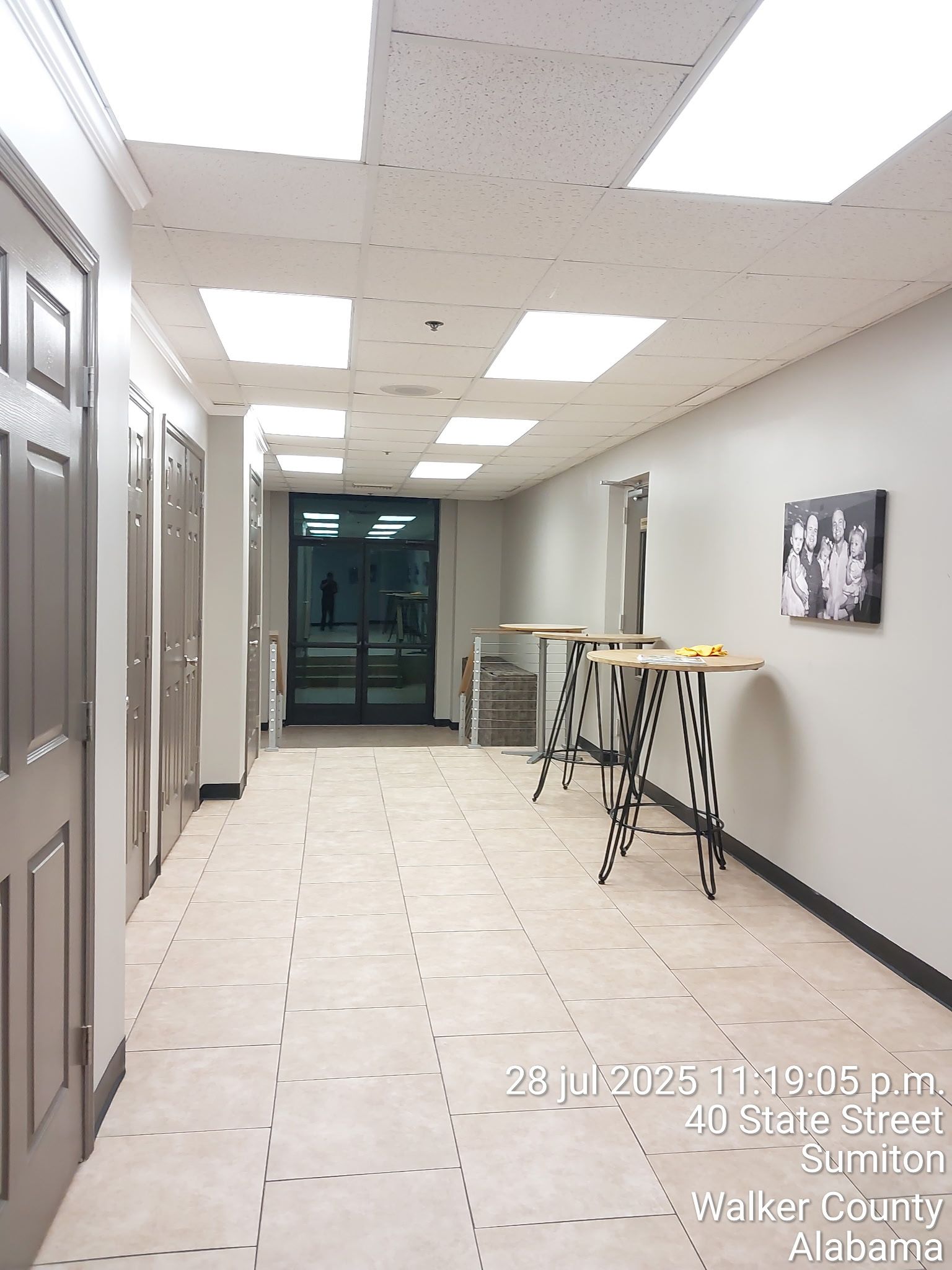 Long office hallway with tiled floor, ceiling lights, doors, and a folding table along the right wall