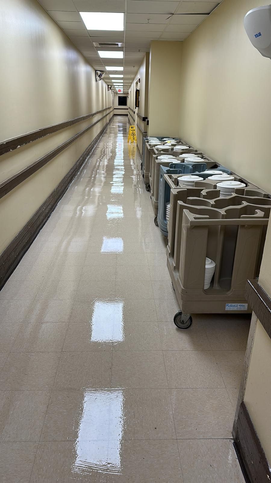 Long hospital hallway with metal utility carts lined along the right side.