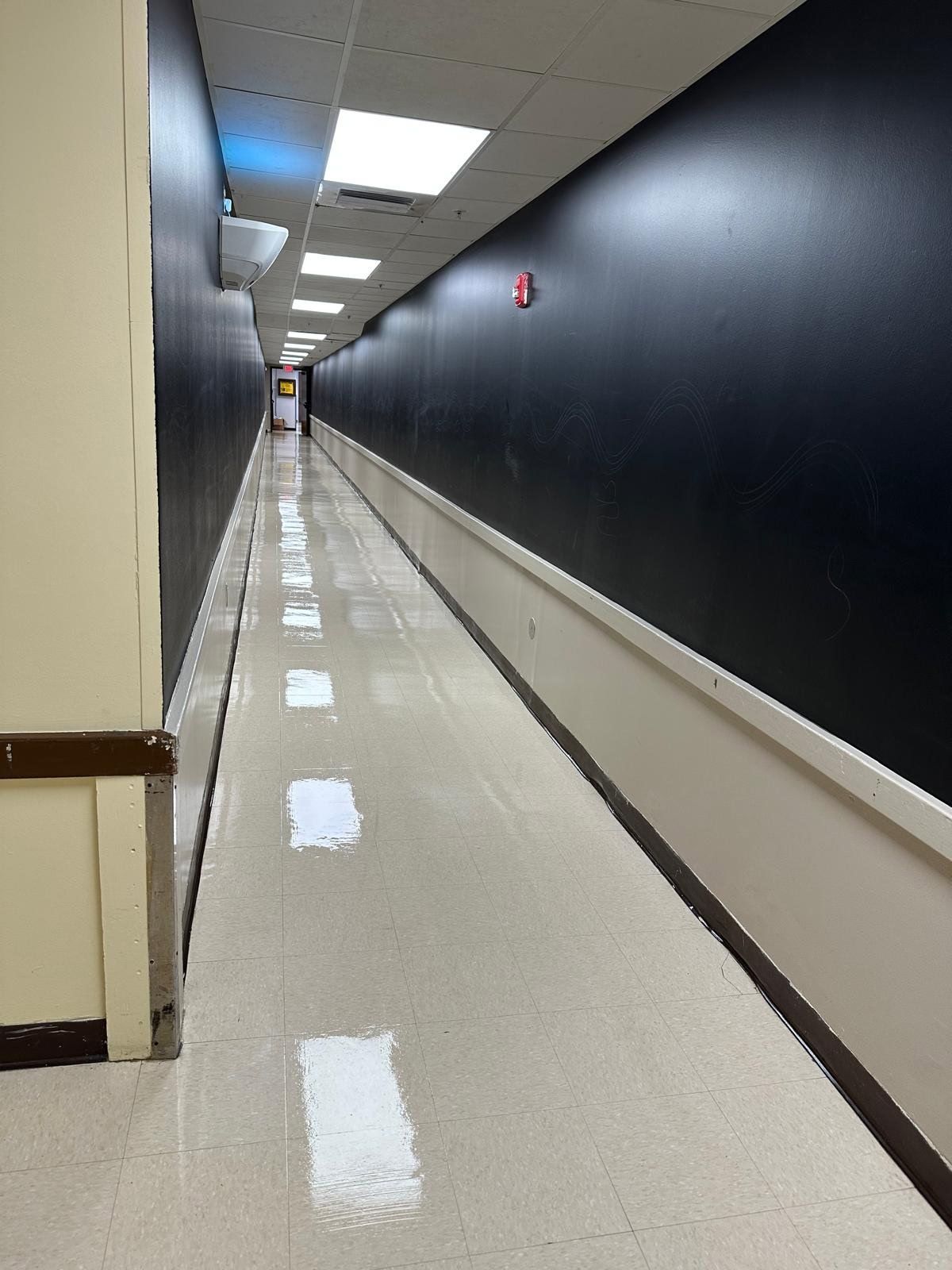 Empty hallway with black walls, white floor, and fluorescent ceiling lights stretching into the distance