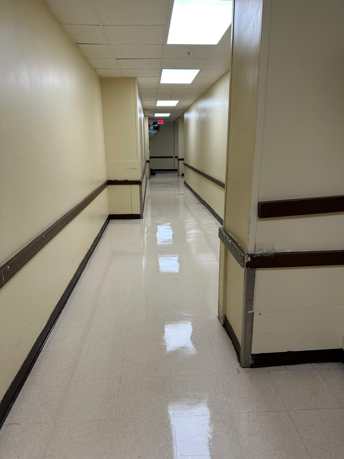 Empty beige hallway with glossy floor, ceiling lights, and dark handrails on both sides