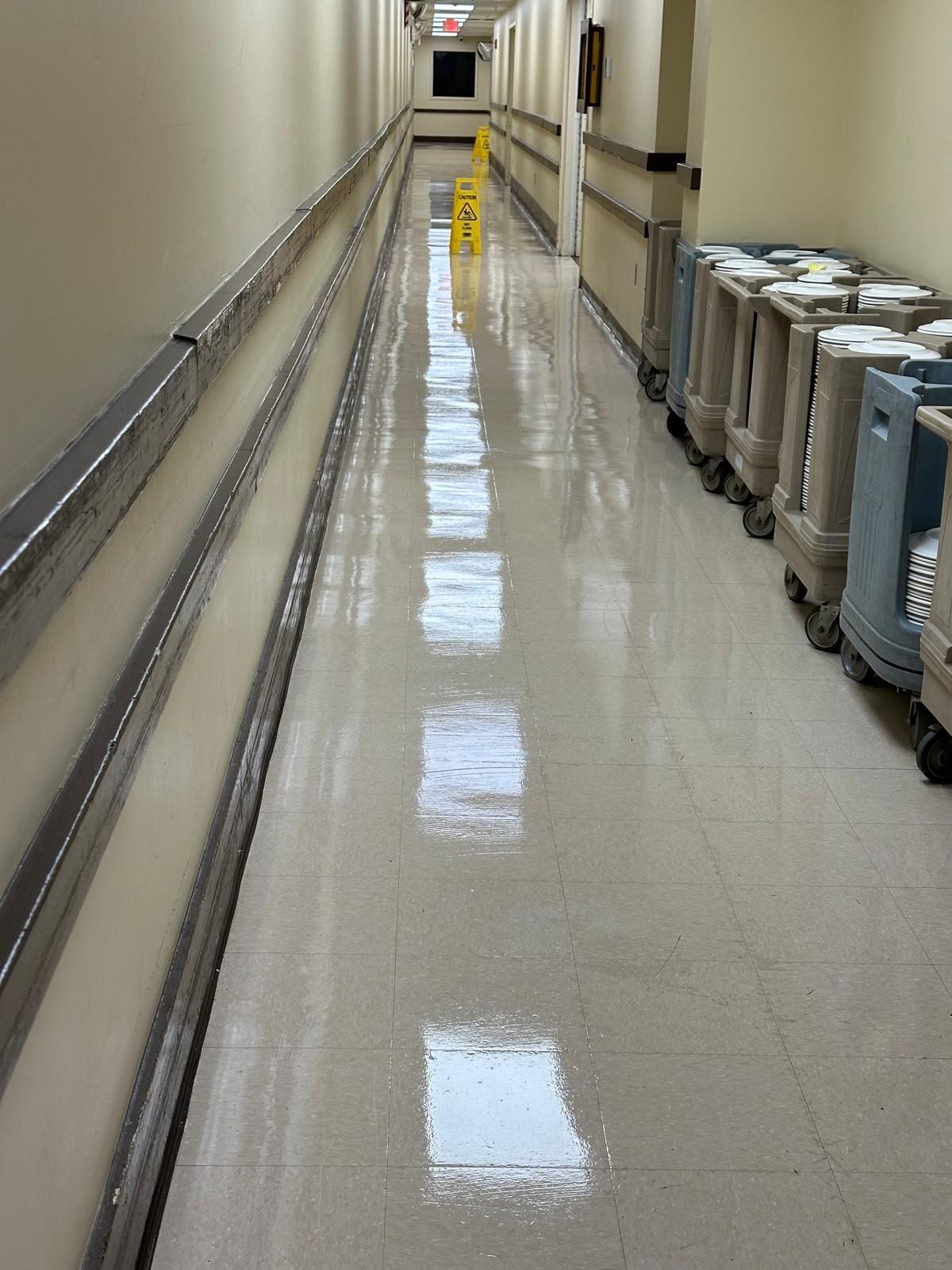Empty hospital hallway with shiny floor and medical equipment lined along the right wall