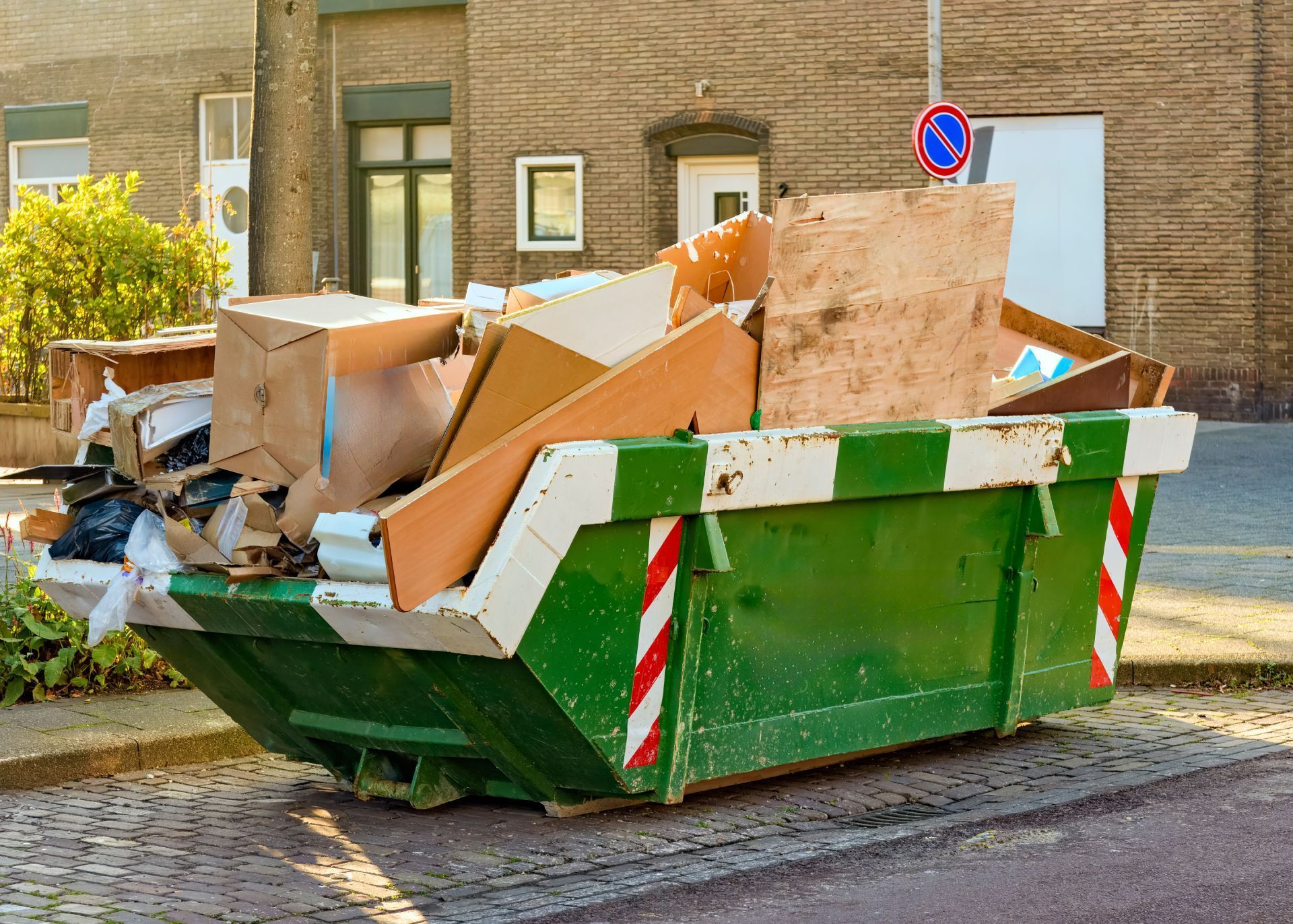 Green dumpster overflowing with cardboard boxes and debris on a residential street